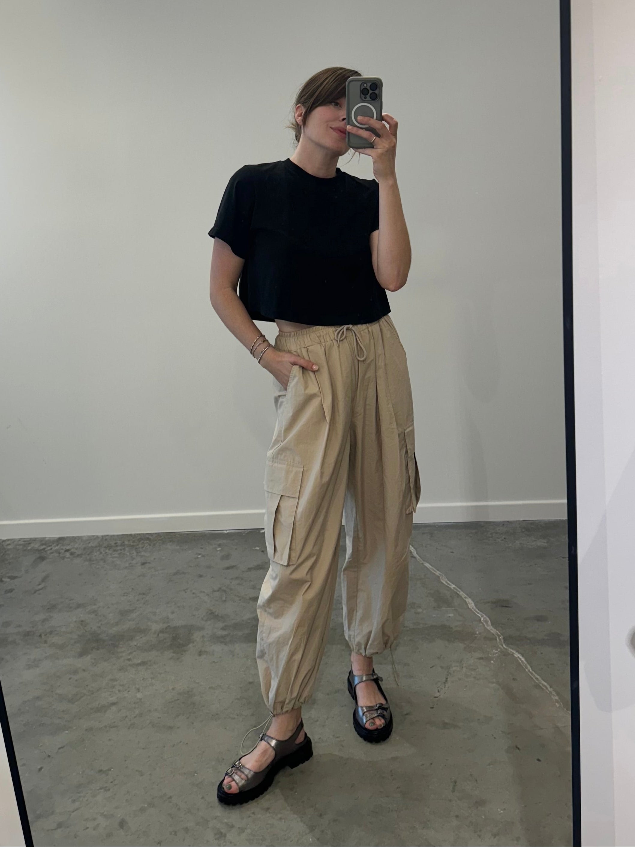 Person wearing a black t-shirt and beige pants taking a mirror selfie.