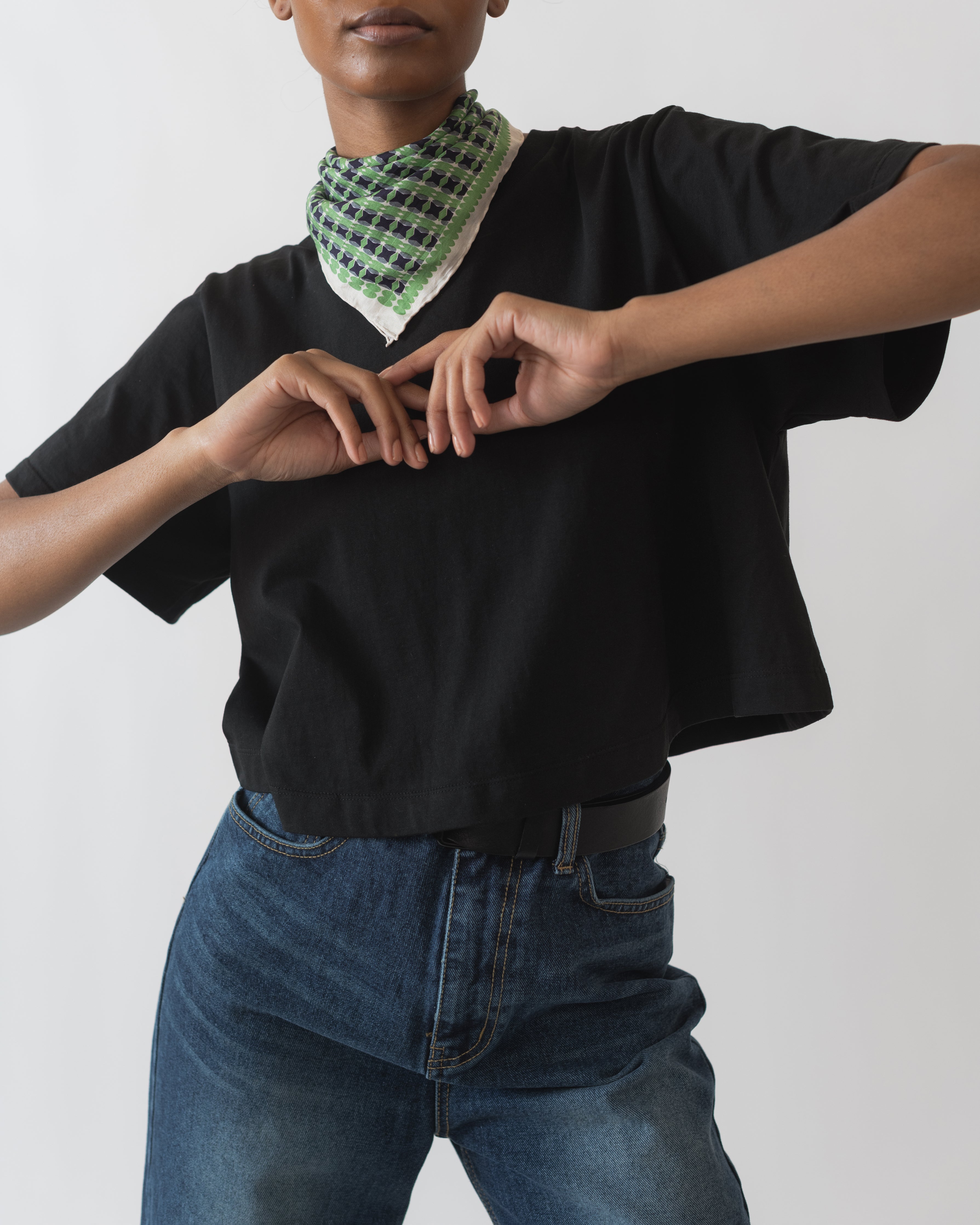 A person wearing a black relaxed cropped t-shirt with a checkered bandana around the neck and blue jeans.