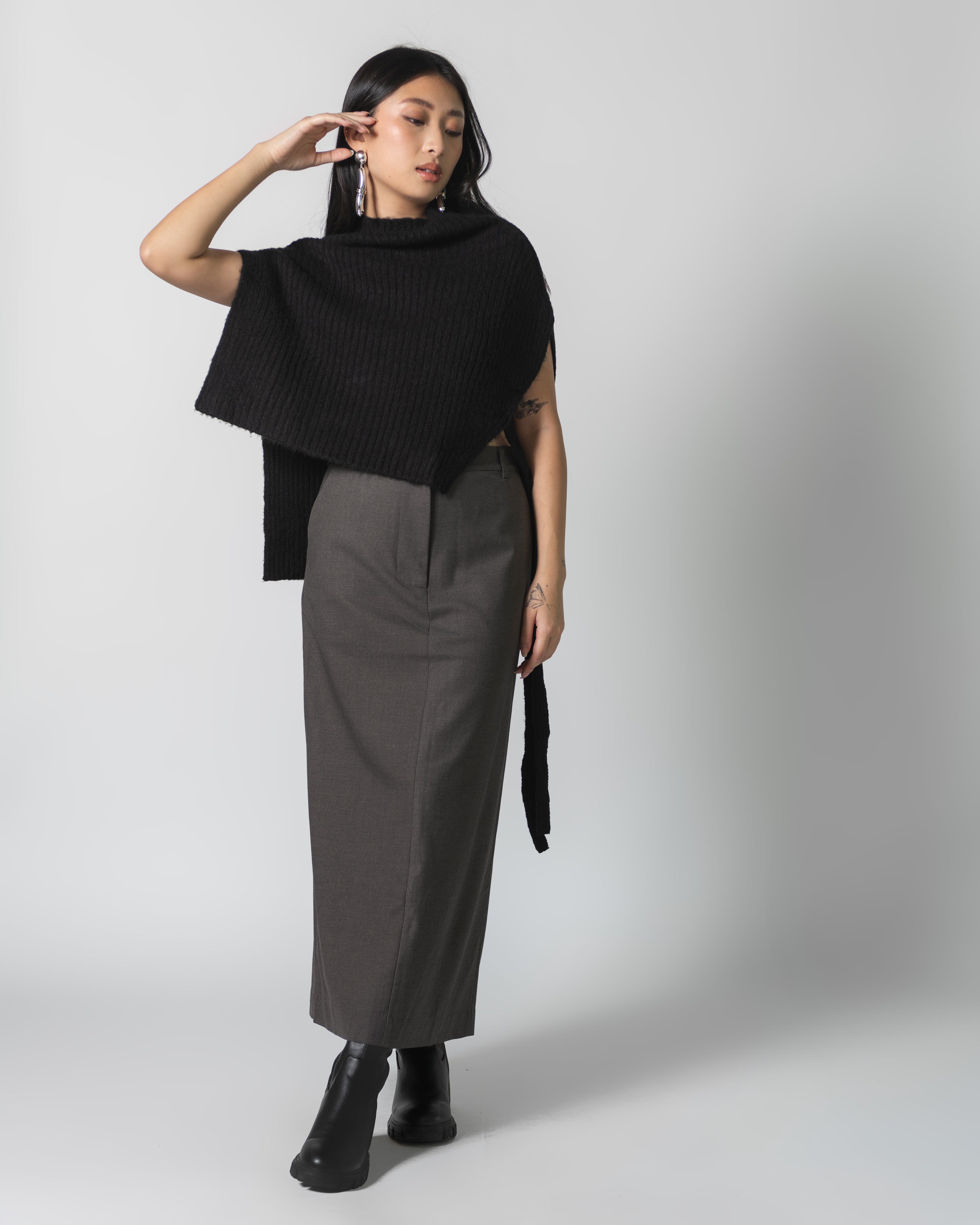 A woman wearing a black ribbed neck warmer cape scarf with a grey maxi skirt at Alas Eius. Fall Fashion inspiration