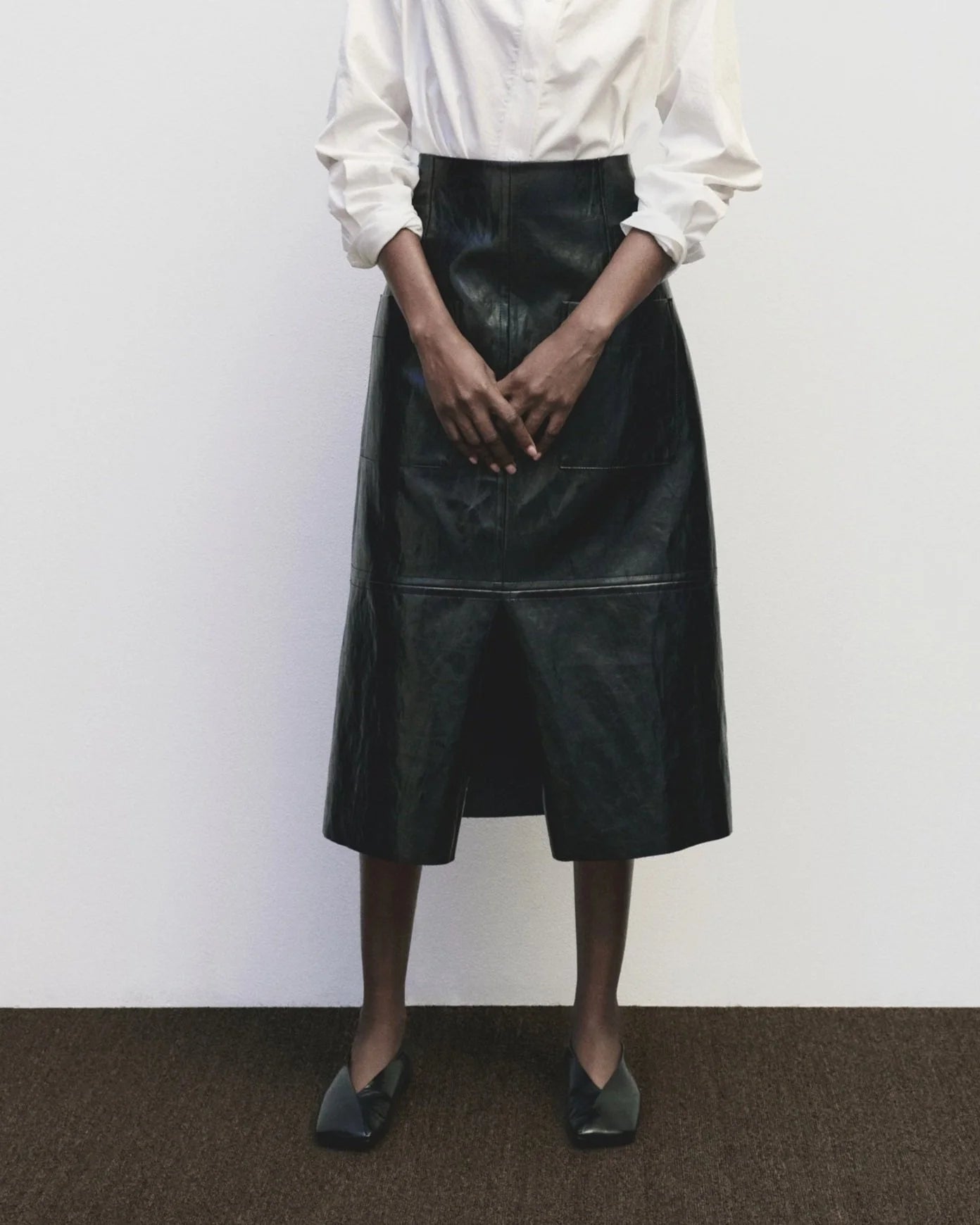 Person wearing a black leather skirt and white shirt against a plain background