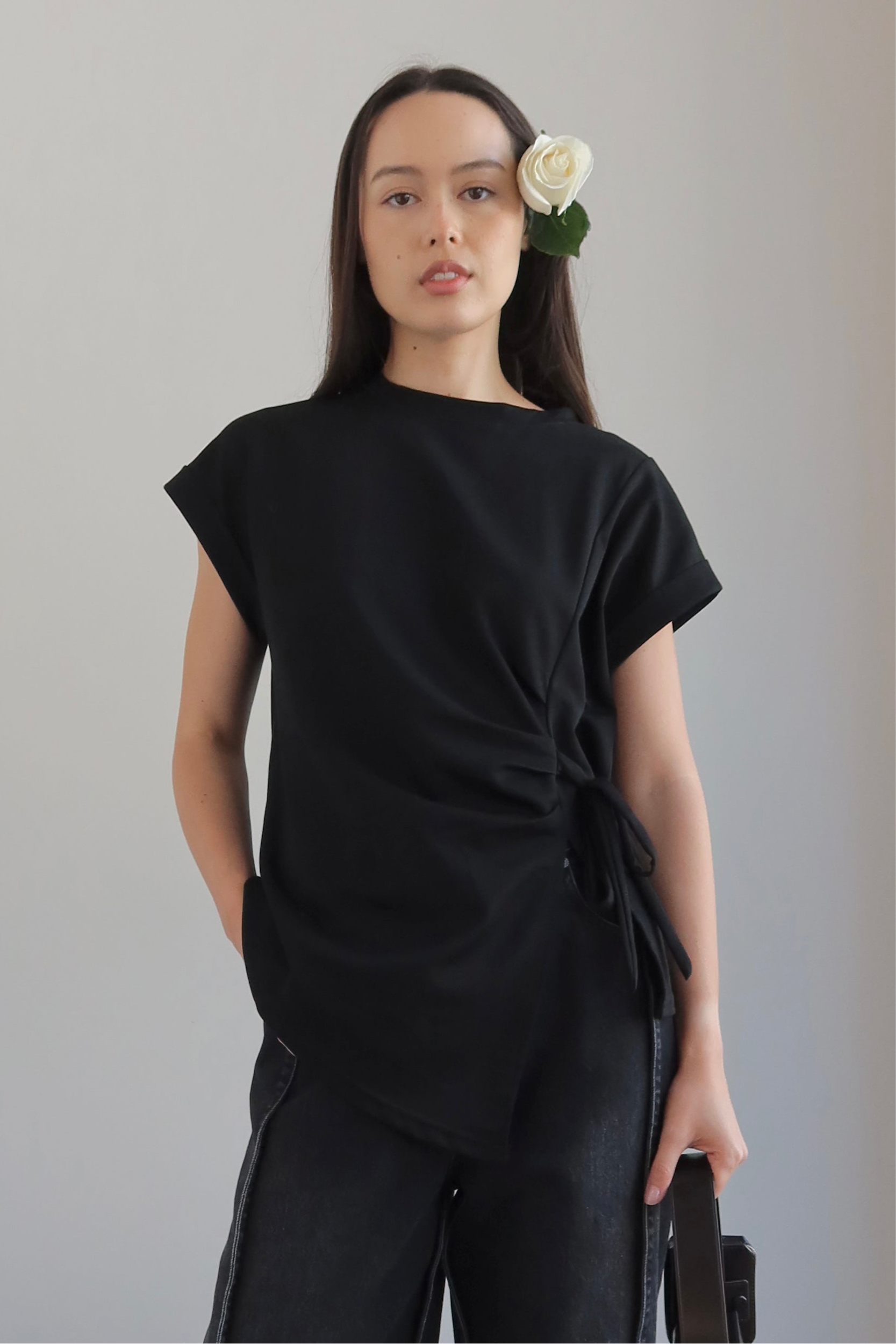 Woman wearing a black outfit with a flower in her hair against a plain background