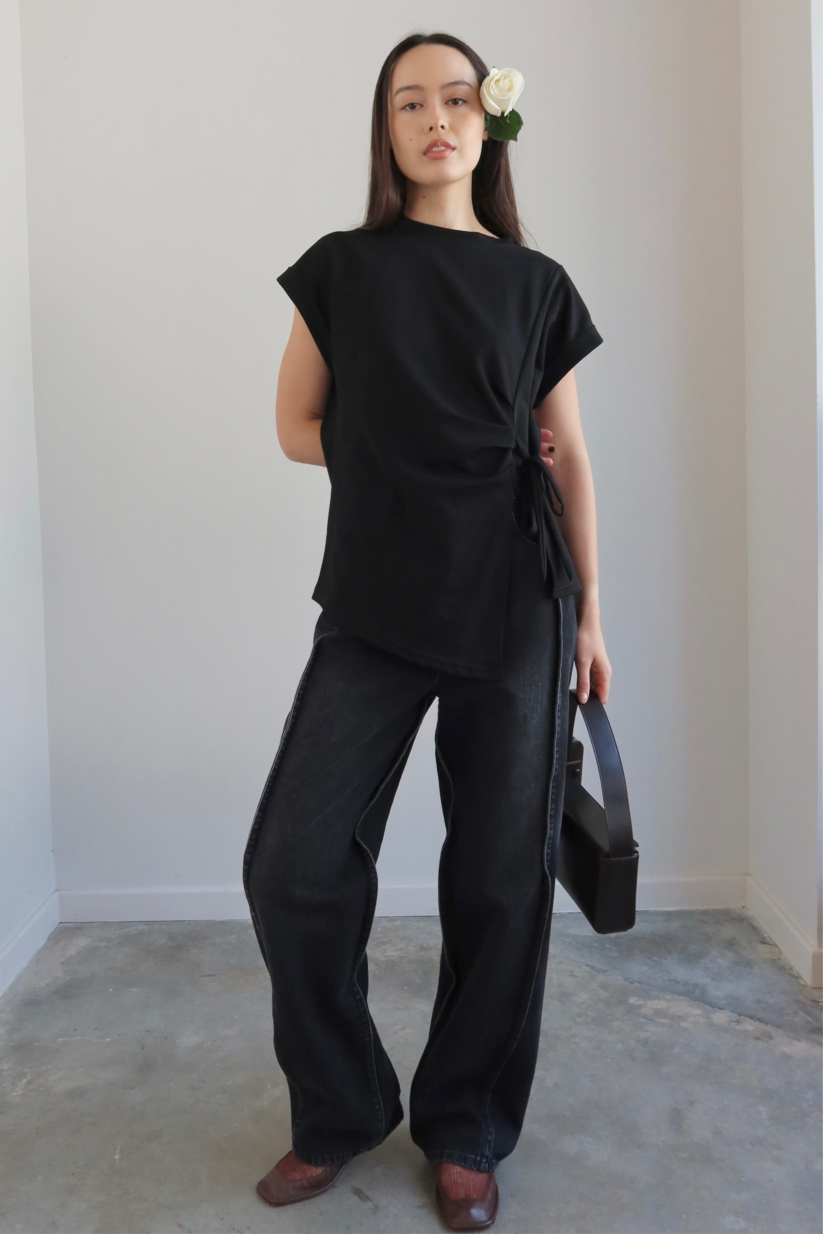 Person wearing a black outfit with wide-leg pants and a black top, holding a black bag.