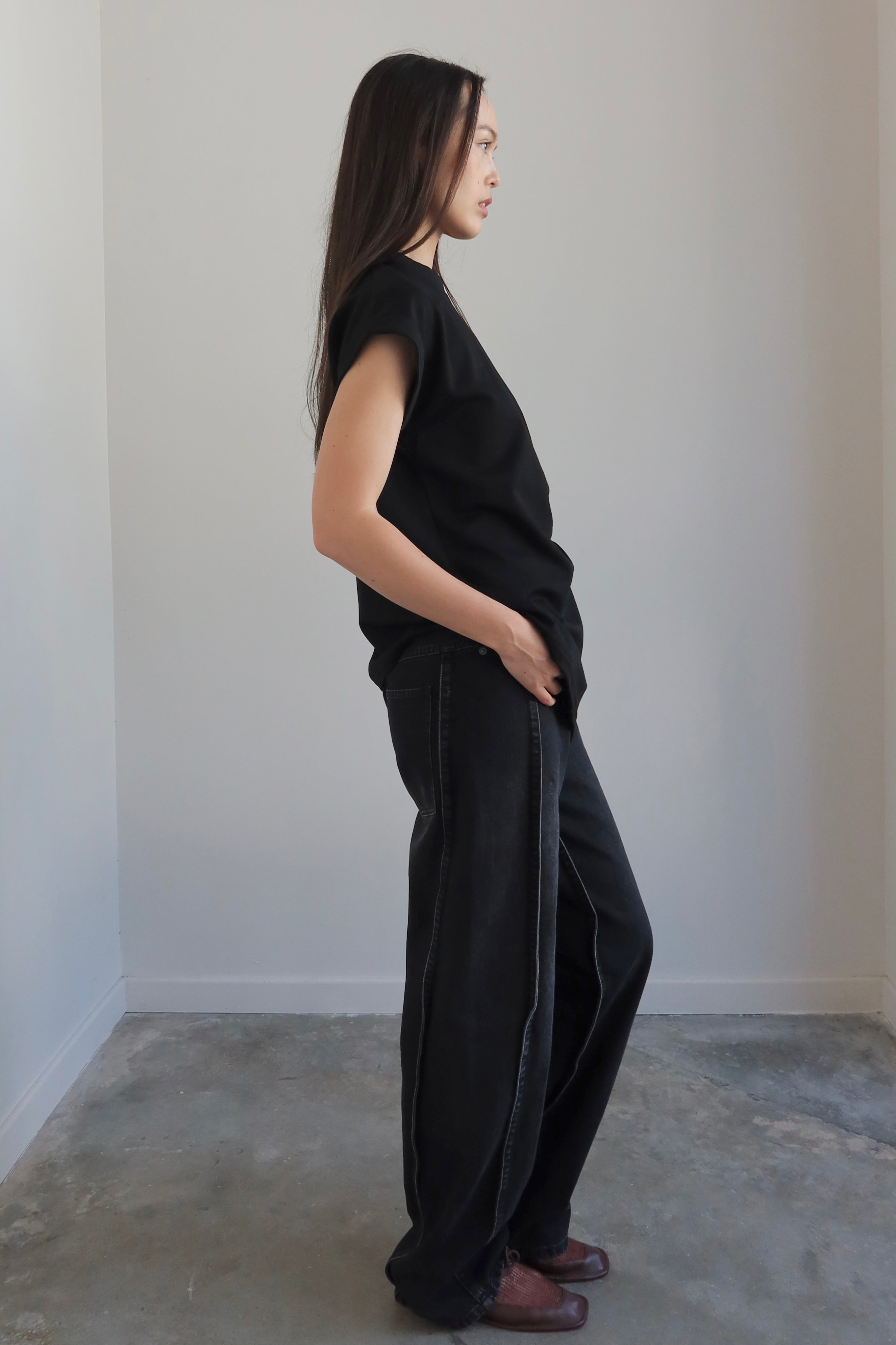 Person wearing a black outfit standing against a plain white wall.