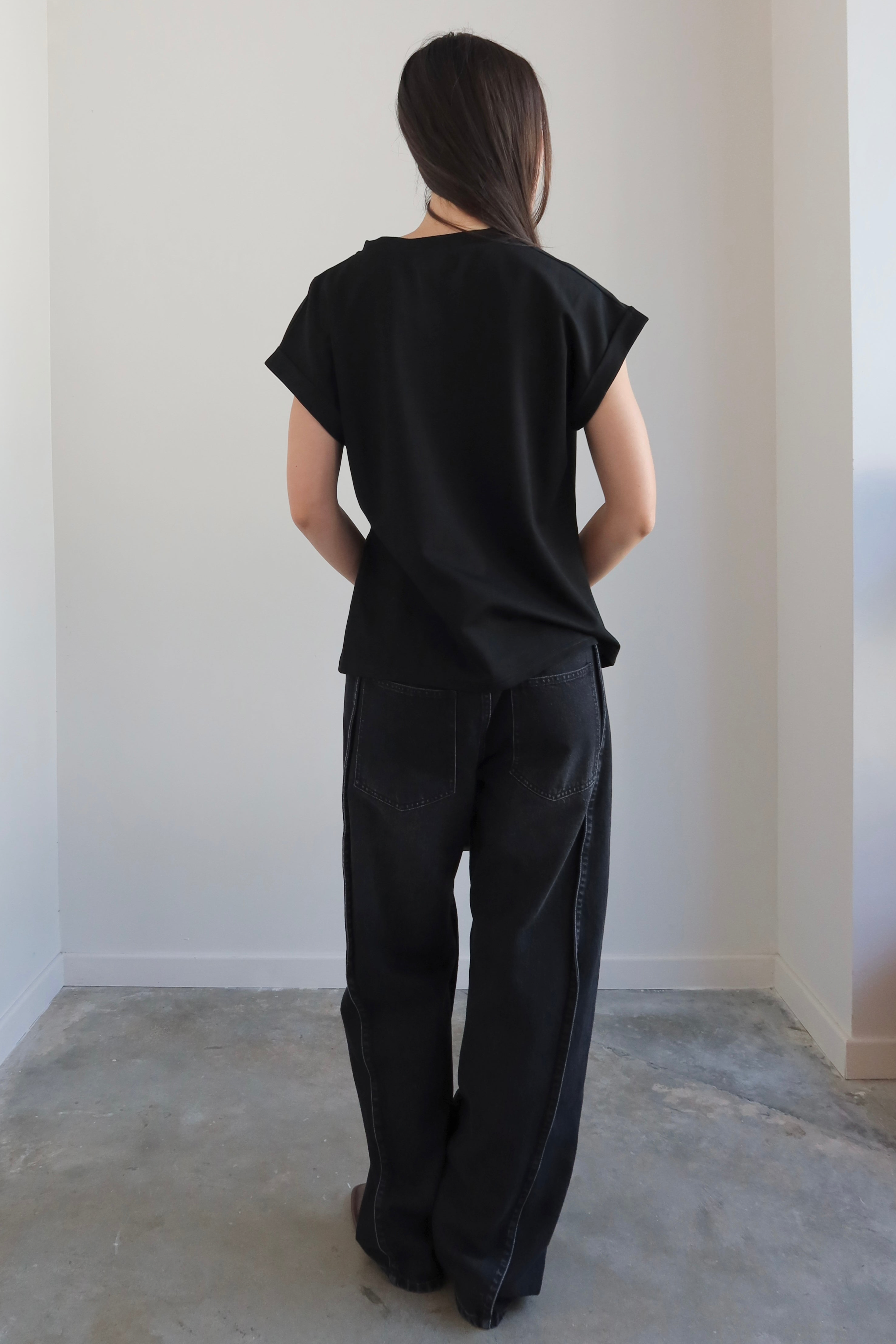 Person wearing a black outfit standing against a white wall.