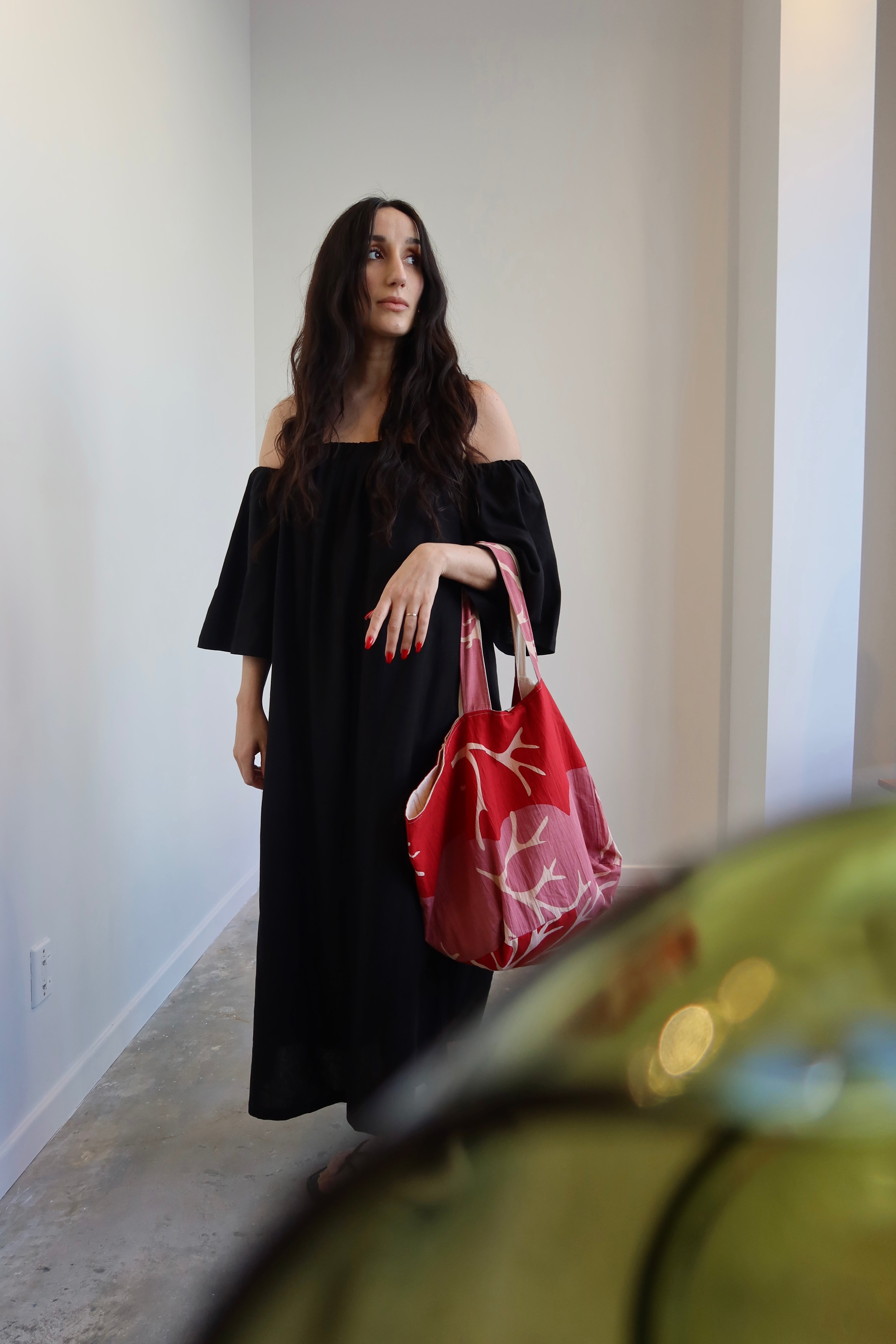 A woman wearing an off-the-shoulder black midi dress with side slant pockets, paired with a red handbag.