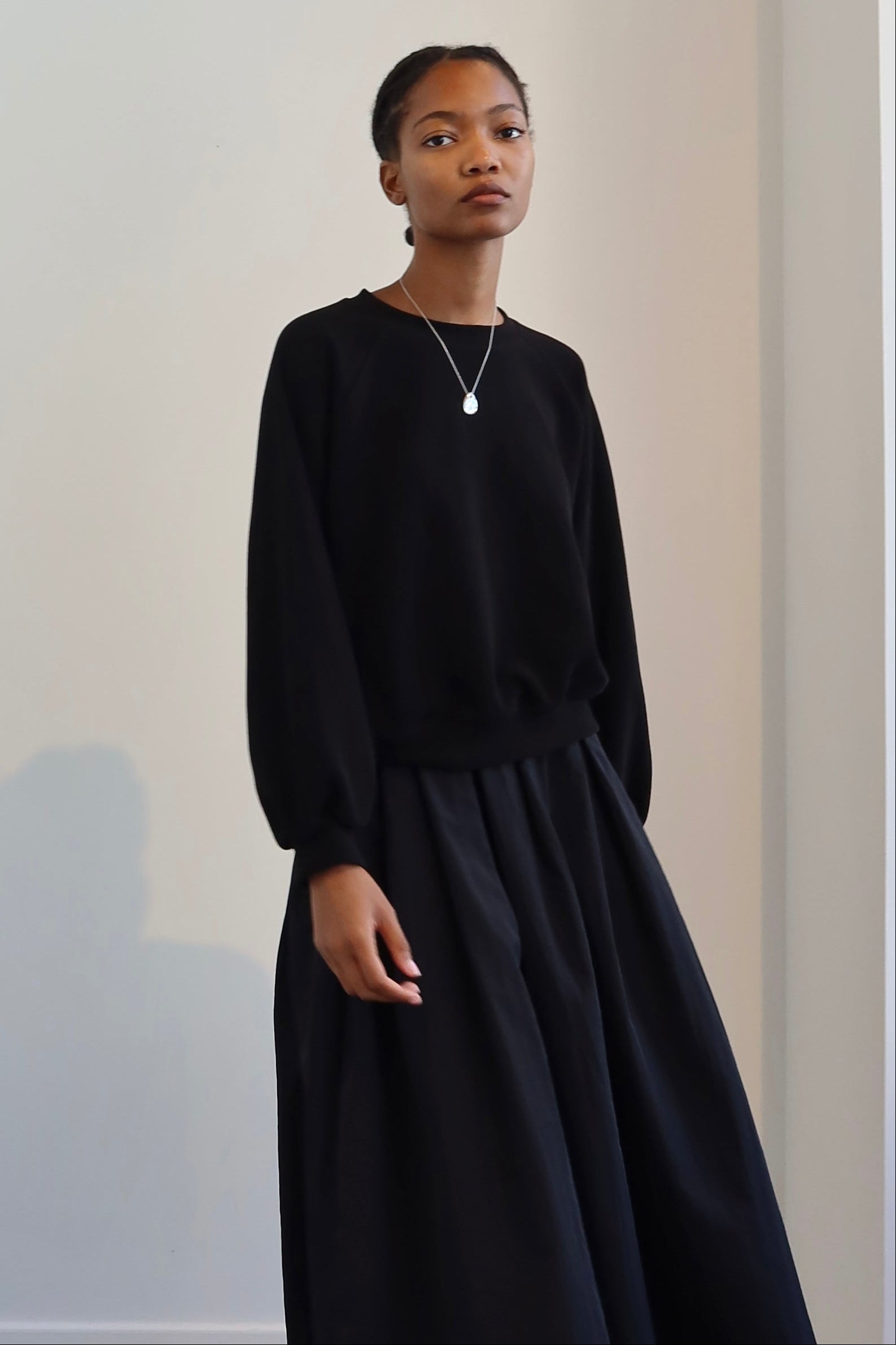 A woman wearing a black raglan sleeve sweatshirt with a round neckline and long sleeves, paired with a dark skirt.