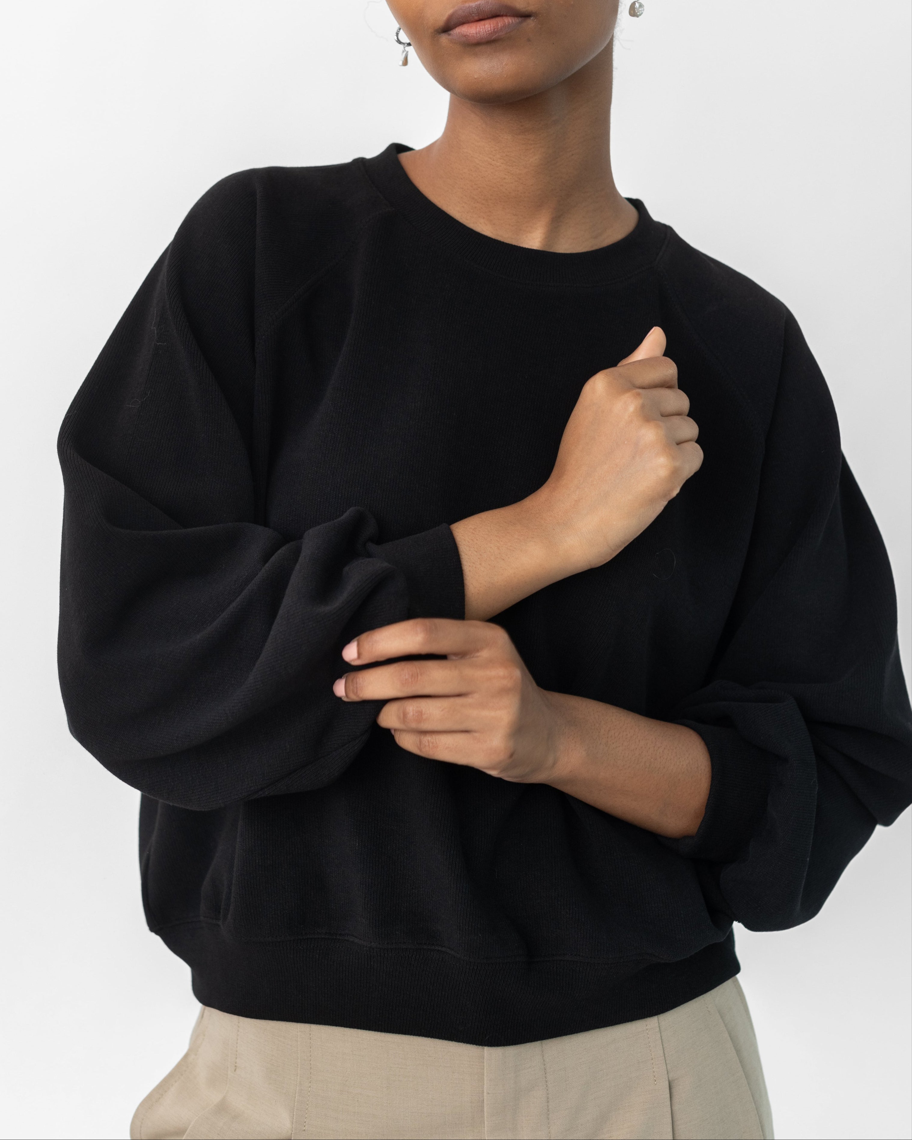 A woman wearing a black raglan sleeve sweatshirt with a round neckline and long sleeves, paired with a dark skirt.