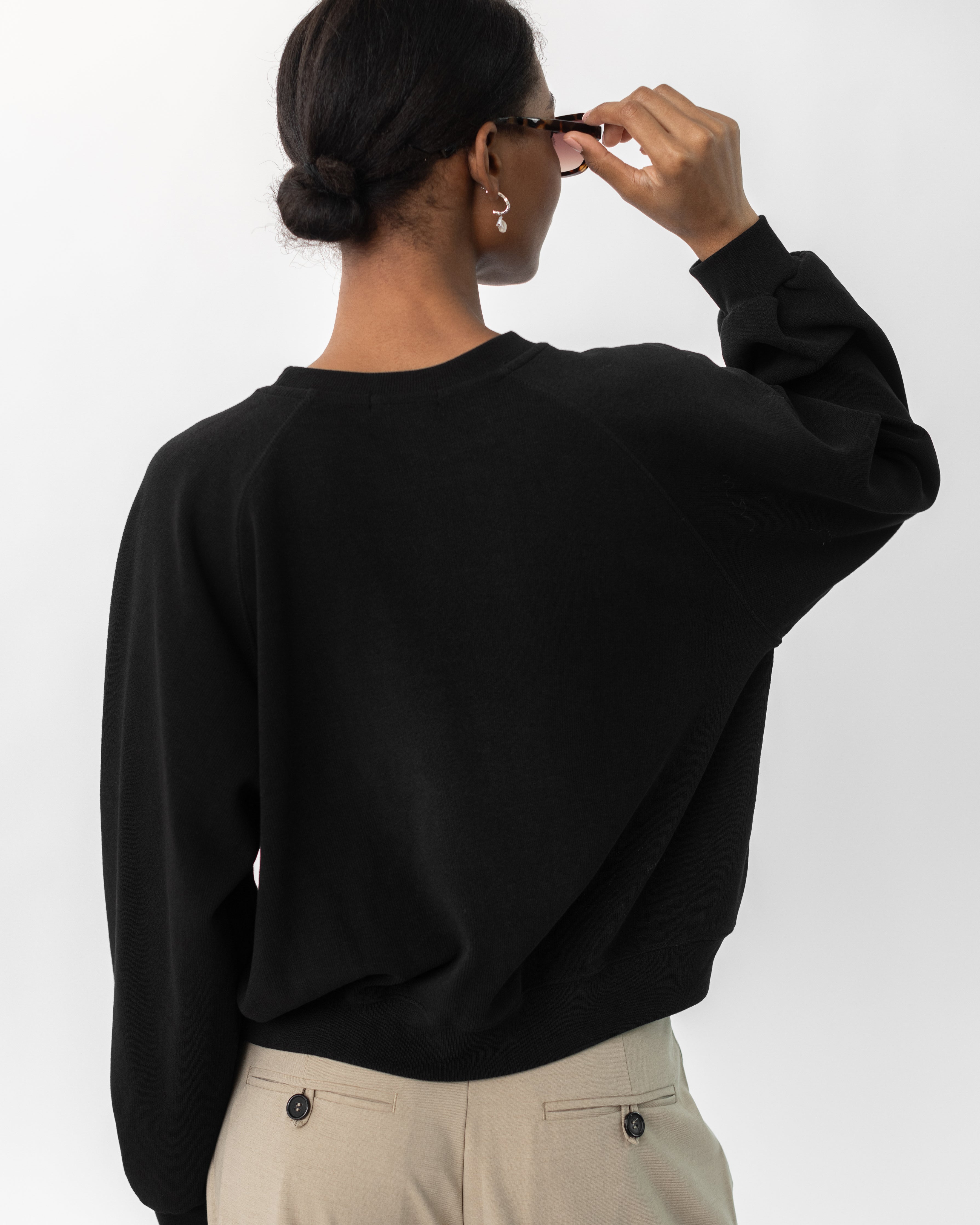 A woman wearing a black raglan sleeve sweatshirt with a round neckline and long sleeves, paired with a dark skirt.
