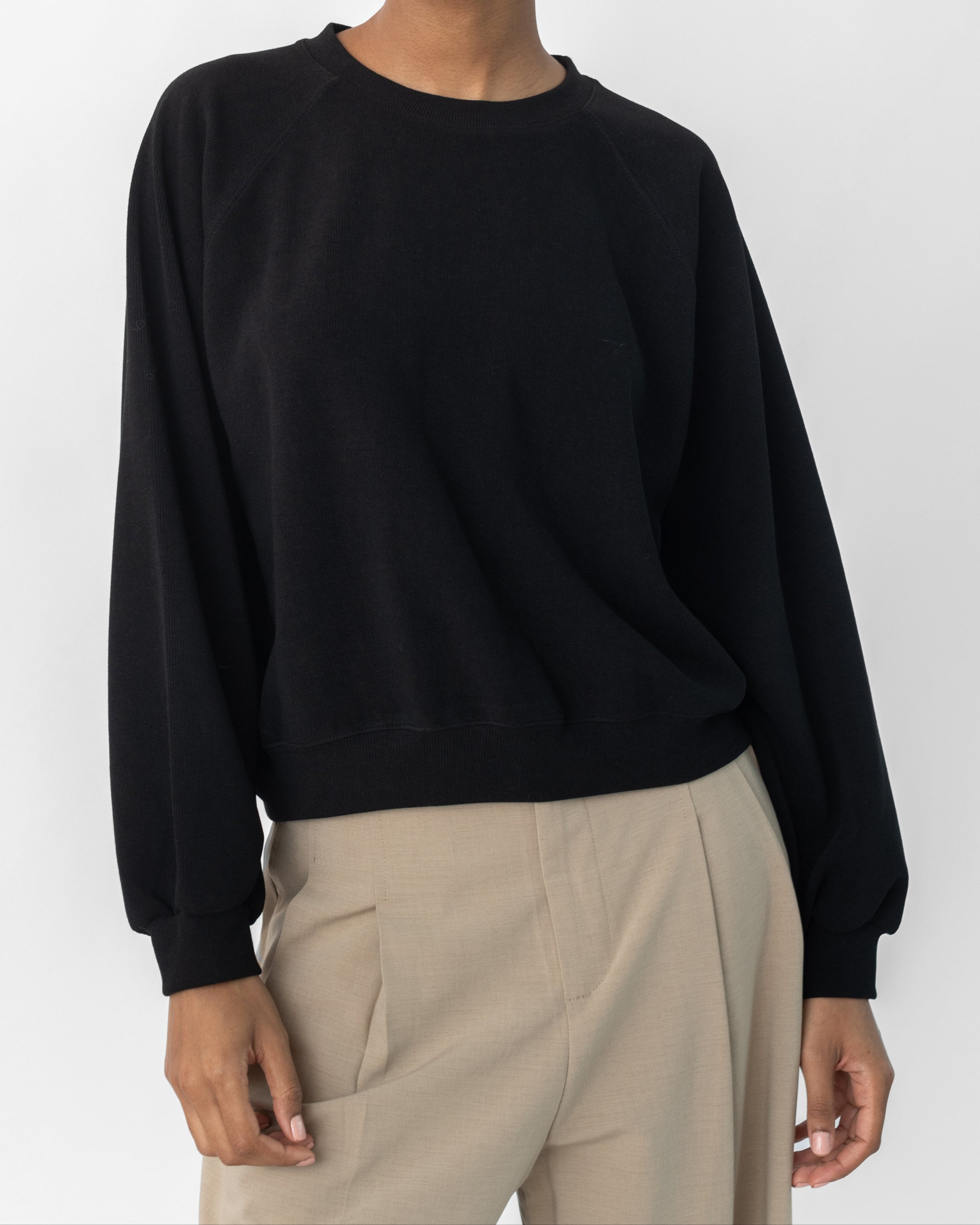 A woman wearing a black raglan sleeve sweatshirt with a round neckline and long sleeves, paired with a dark skirt.