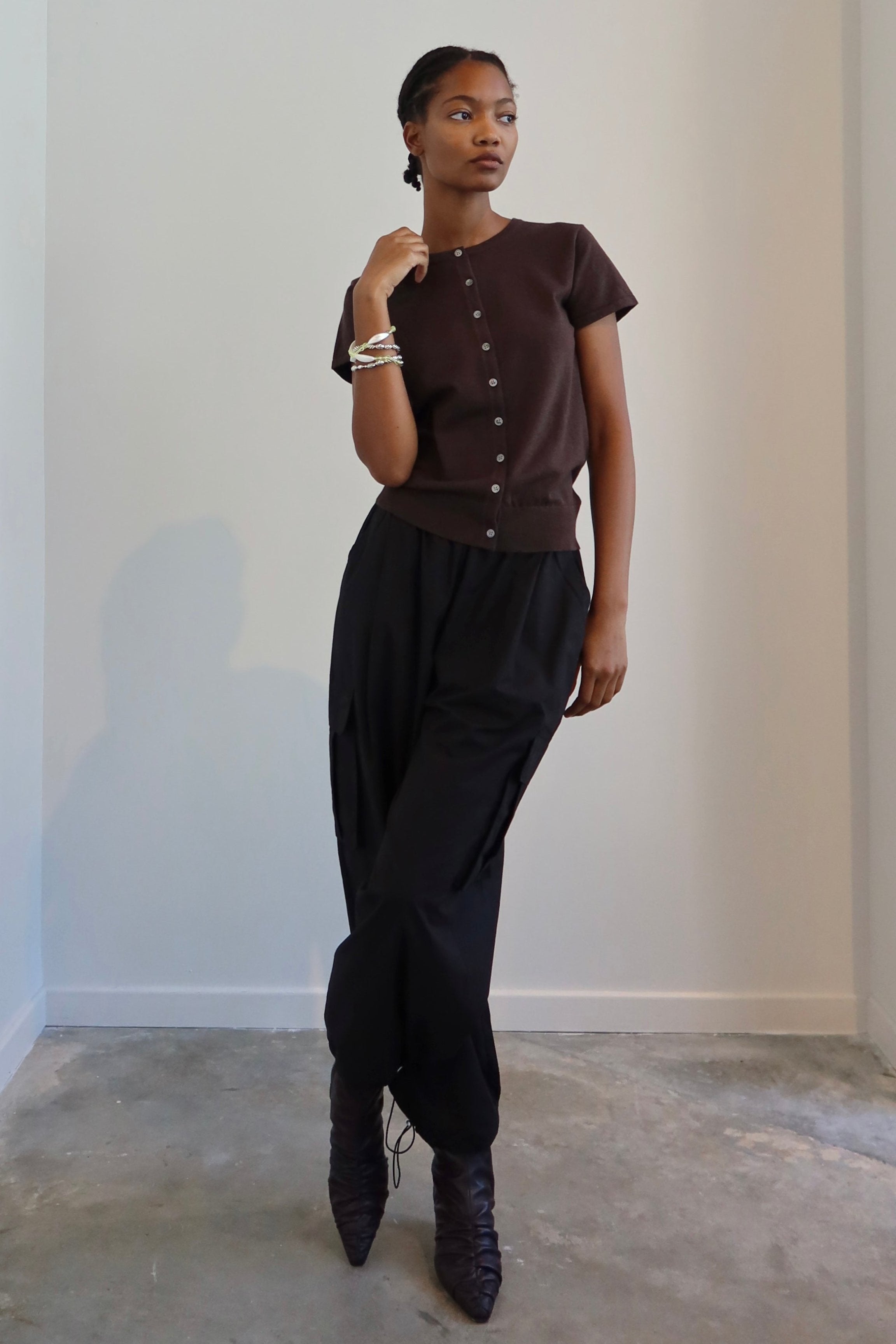 A person standing in a neutral pose wearing black wide-leg cargo pants with a drawstring waist, paired with a brown top and boots.