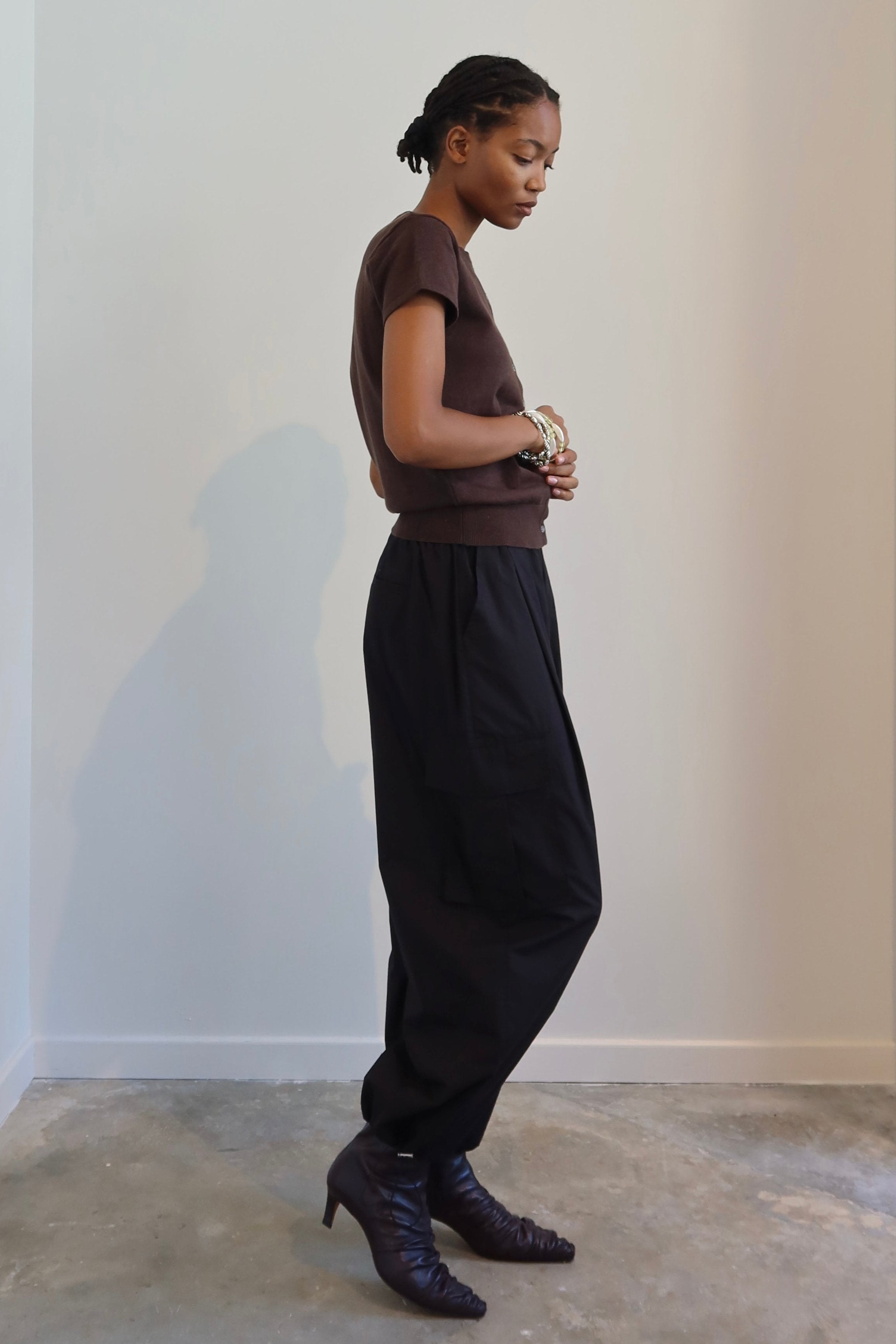 A person standing in a neutral pose wearing black wide-leg cargo pants with a drawstring waist, paired with a brown top and boots.