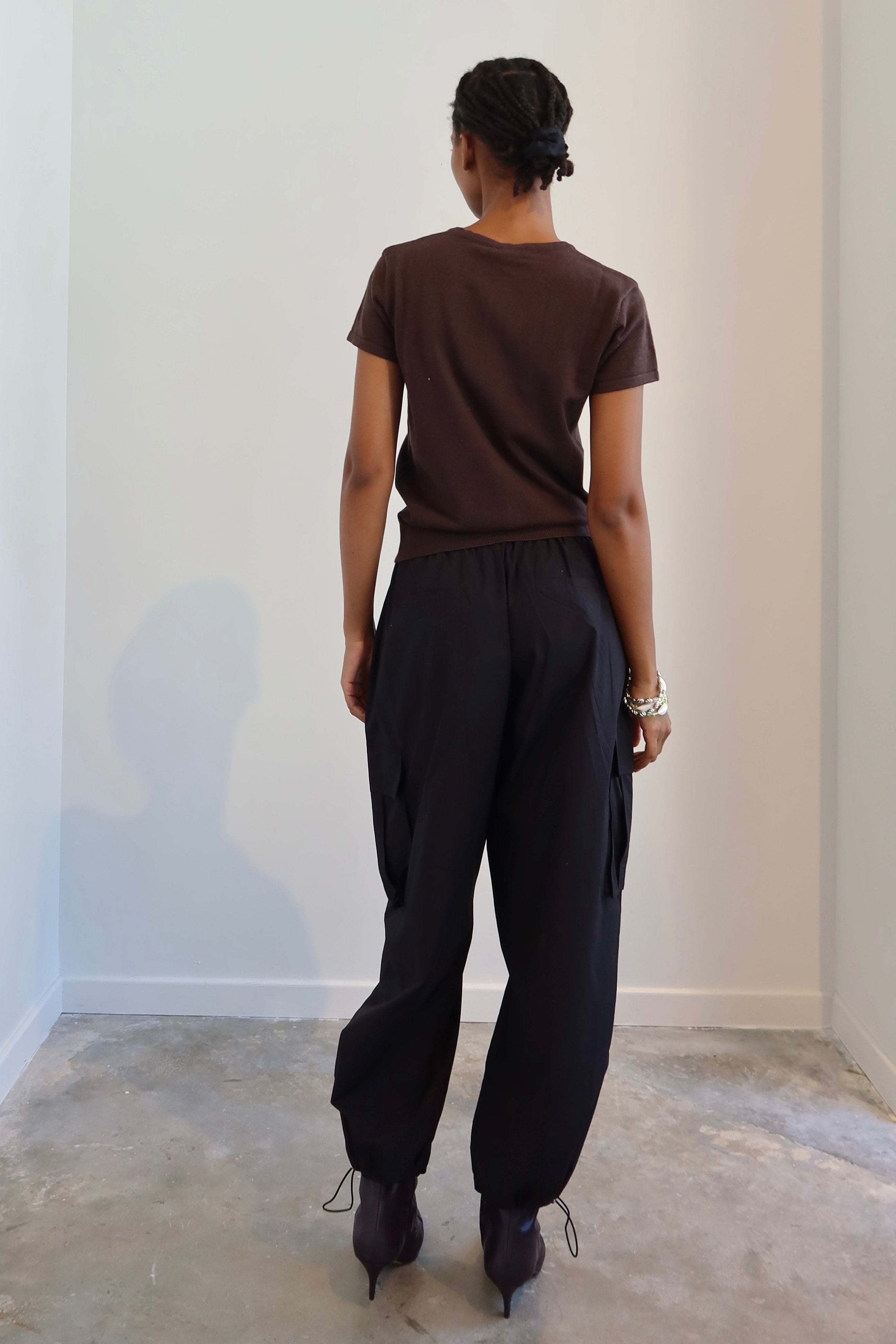 A person standing in a neutral pose wearing black wide-leg cargo pants with a drawstring waist, paired with a brown top and boots.