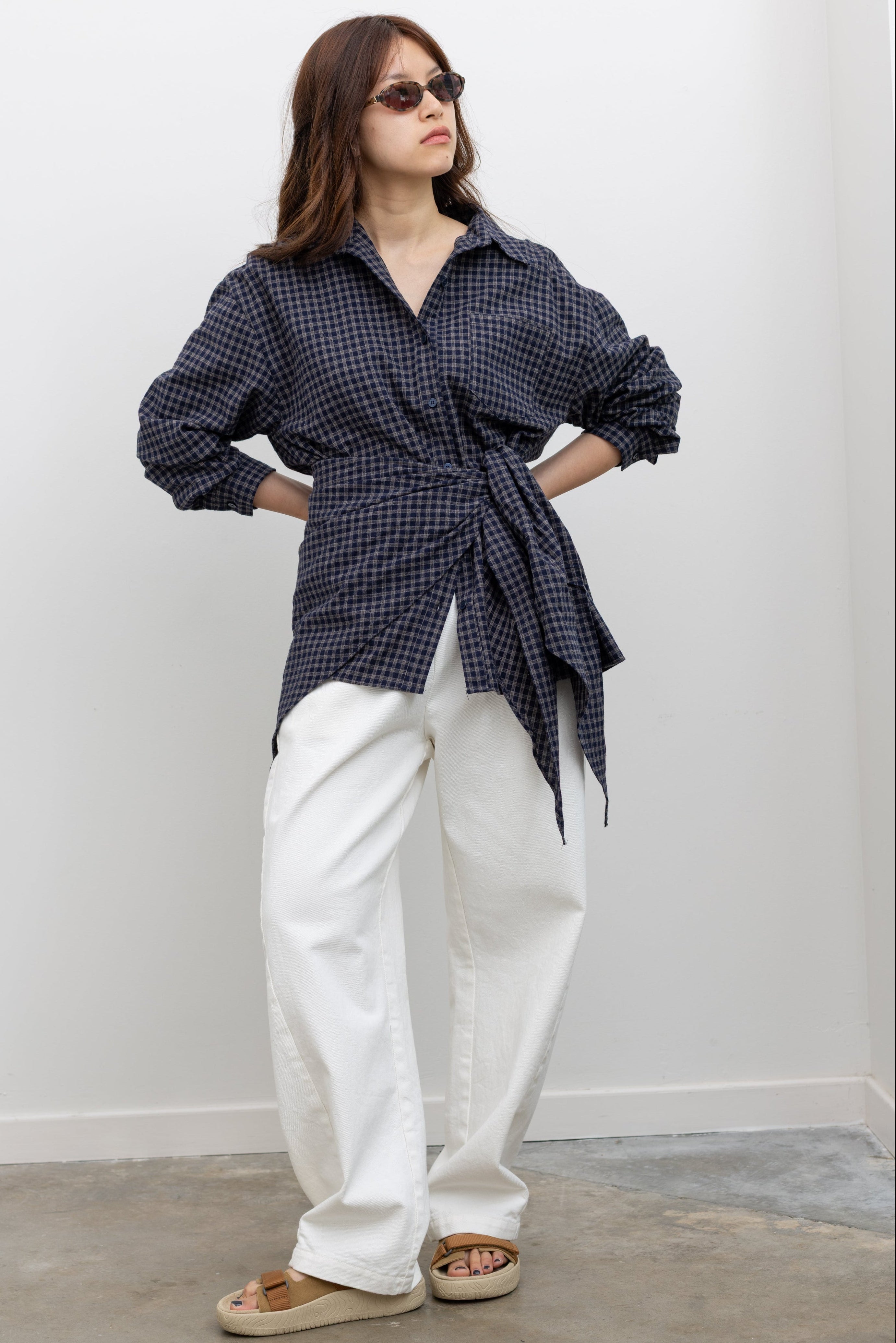 Alas Eius label oversized navy blue and tan plaid button-down top styled with coordinating bandana scarf around waist for a flattering cinched look paired with white denim jeans at Alas Eius. 