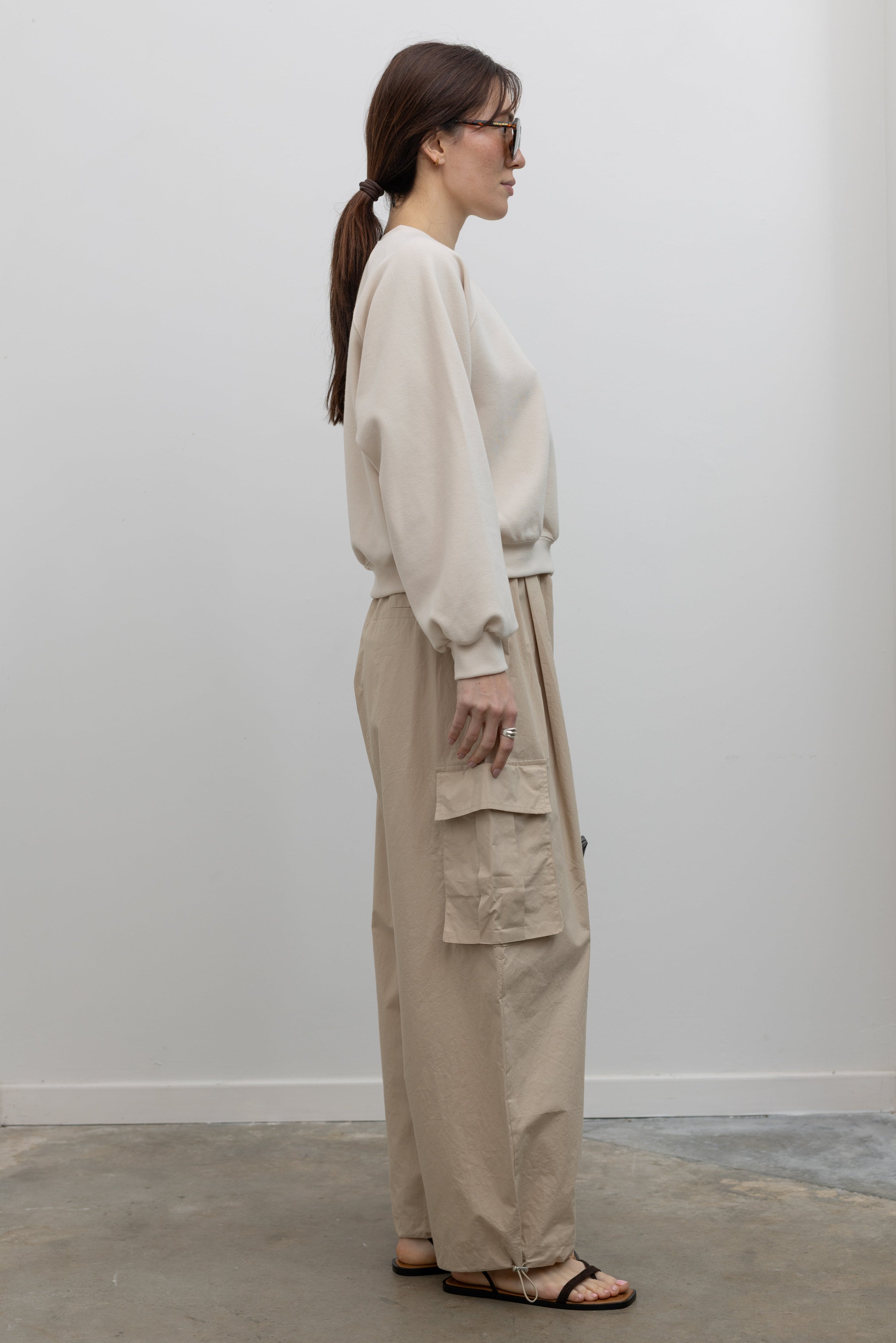 Side view of Woman wearing Alas Eius Brand Cream Raglan long-sleeved crewneck Sweatshirt with khaki cargo pants and sunglasses at Alas Eius