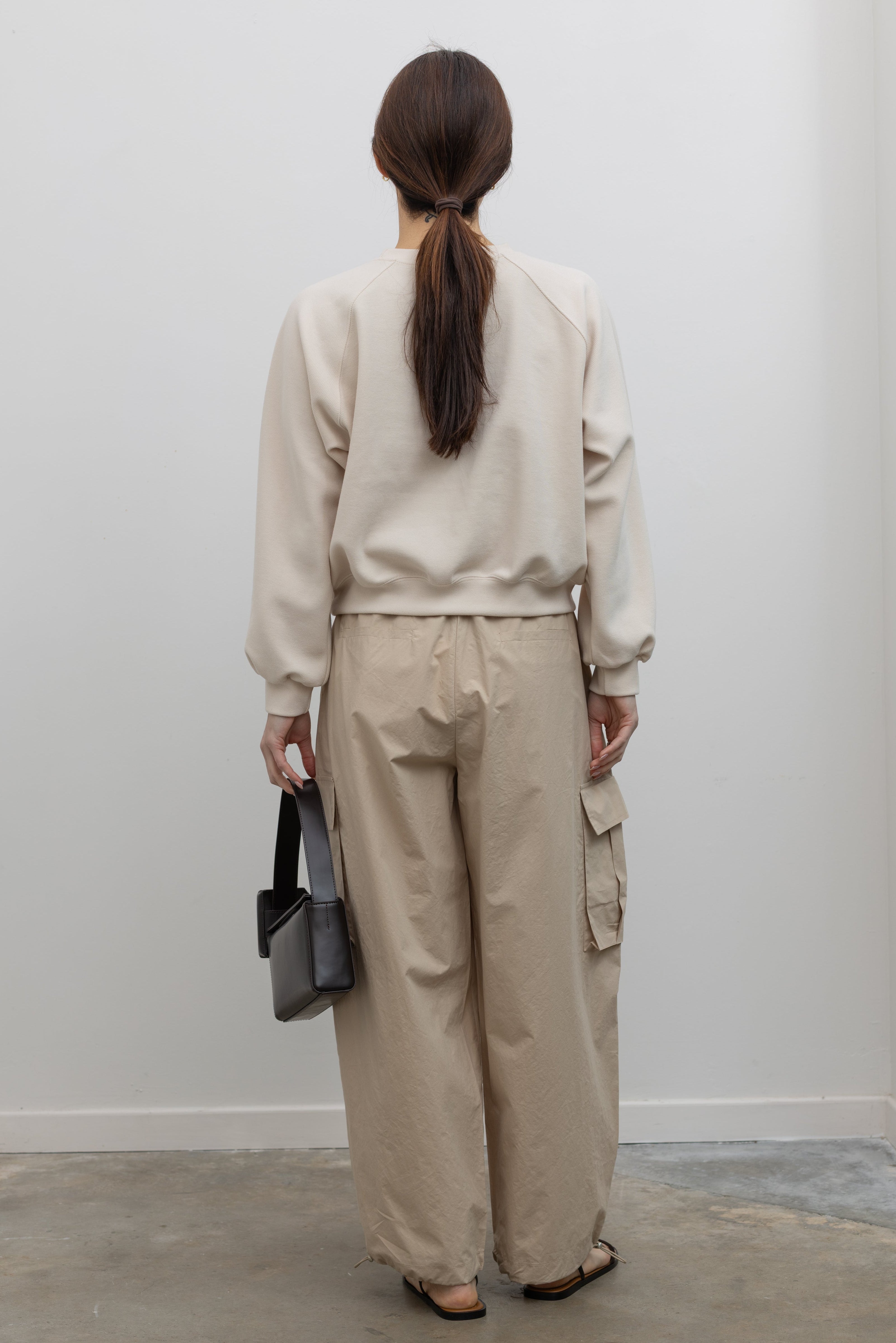 Back view of Woman wearing Alas Eius Brand Cream Raglan long-sleeved crewneck Sweatshirt with khaki cargo pants and sunglasses at Alas Eius