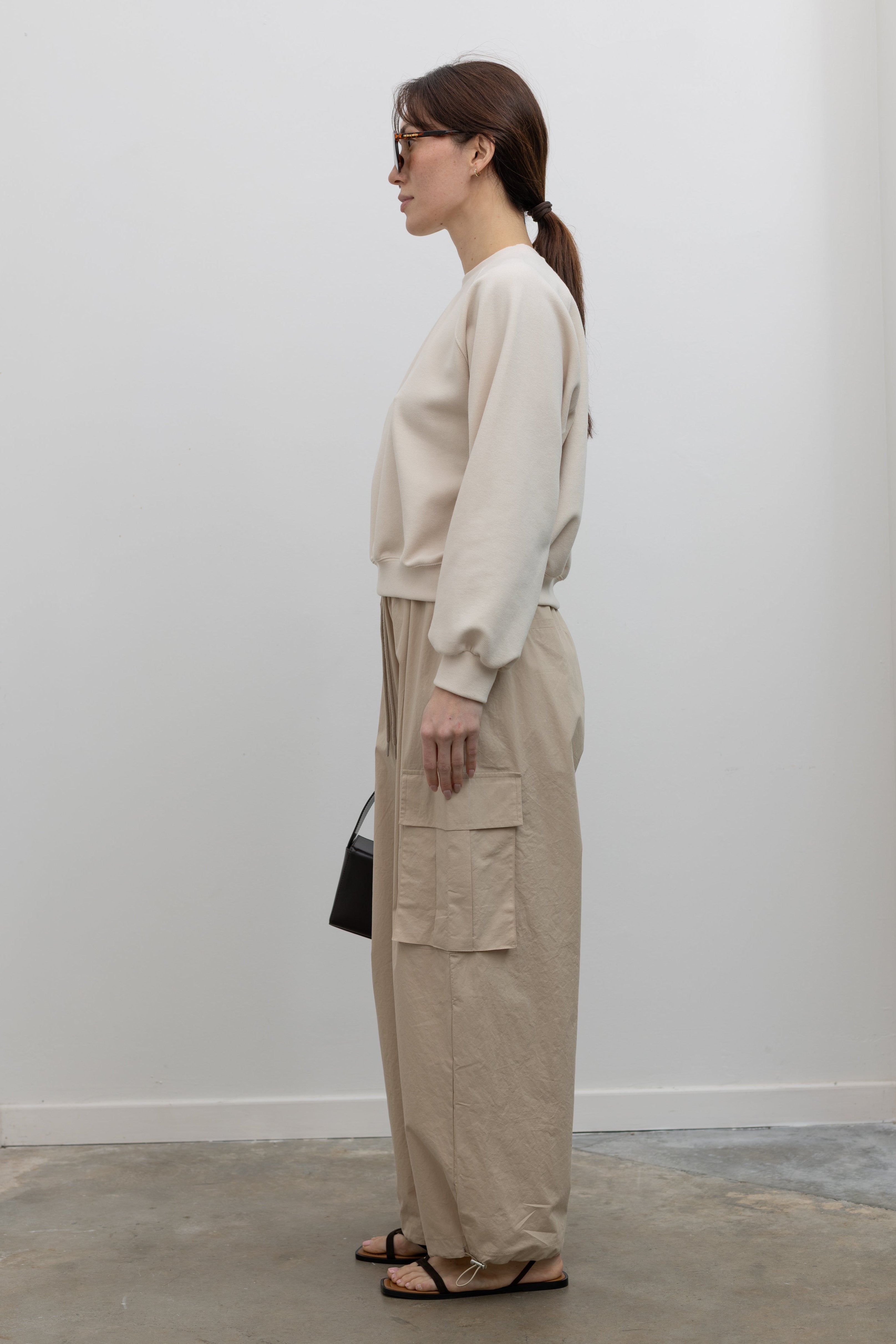 Side view of Woman wearing Alas Eius Brand Cream Raglan long-sleeved crewneck Sweatshirt with khaki cargo pants and sunglasses at Alas Eius