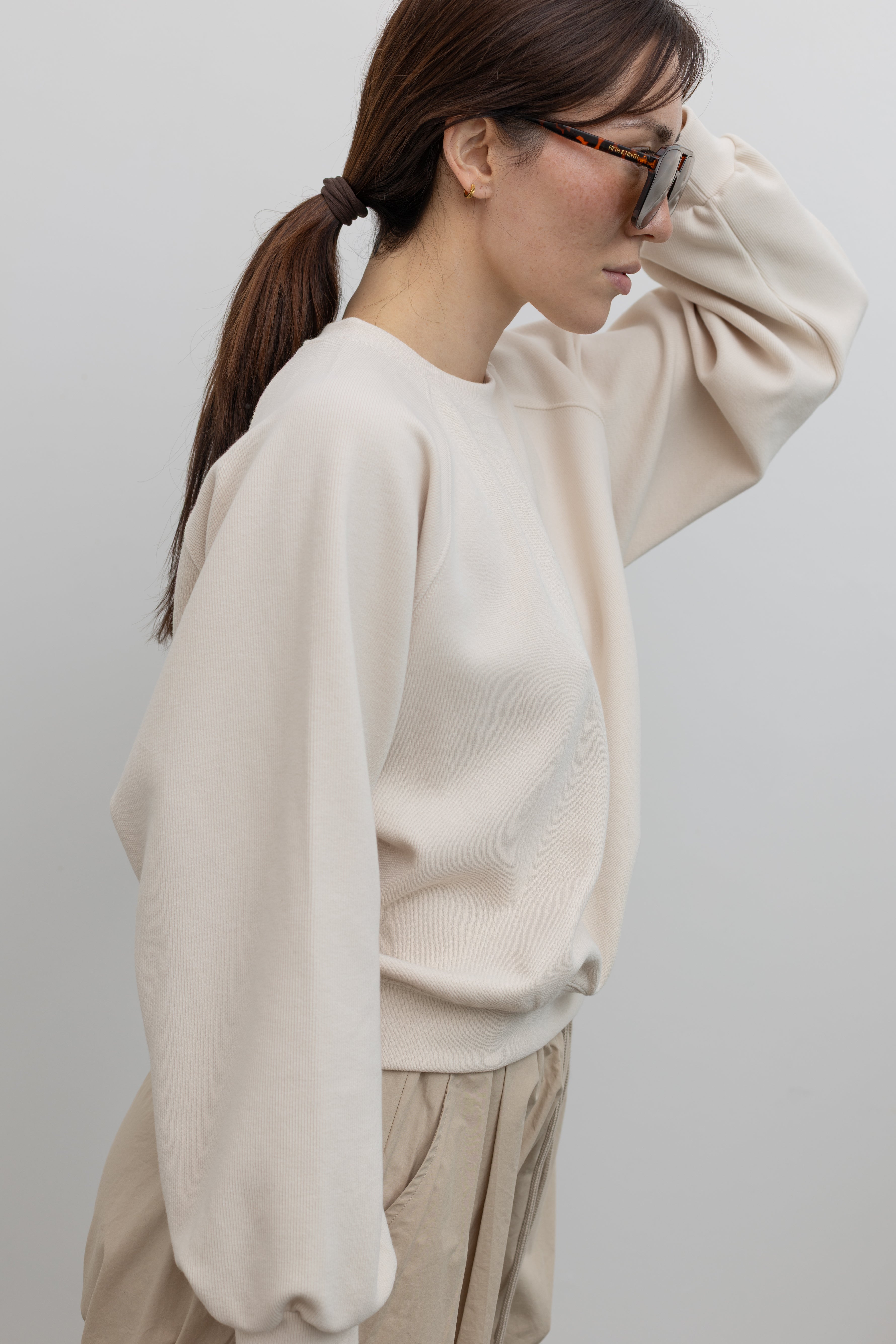 Detailed product view of Woman wearing Alas Eius Brand Cream Raglan long-sleeved crewneck Sweatshirt with khaki cargo pants and sunglasses at Alas Eius