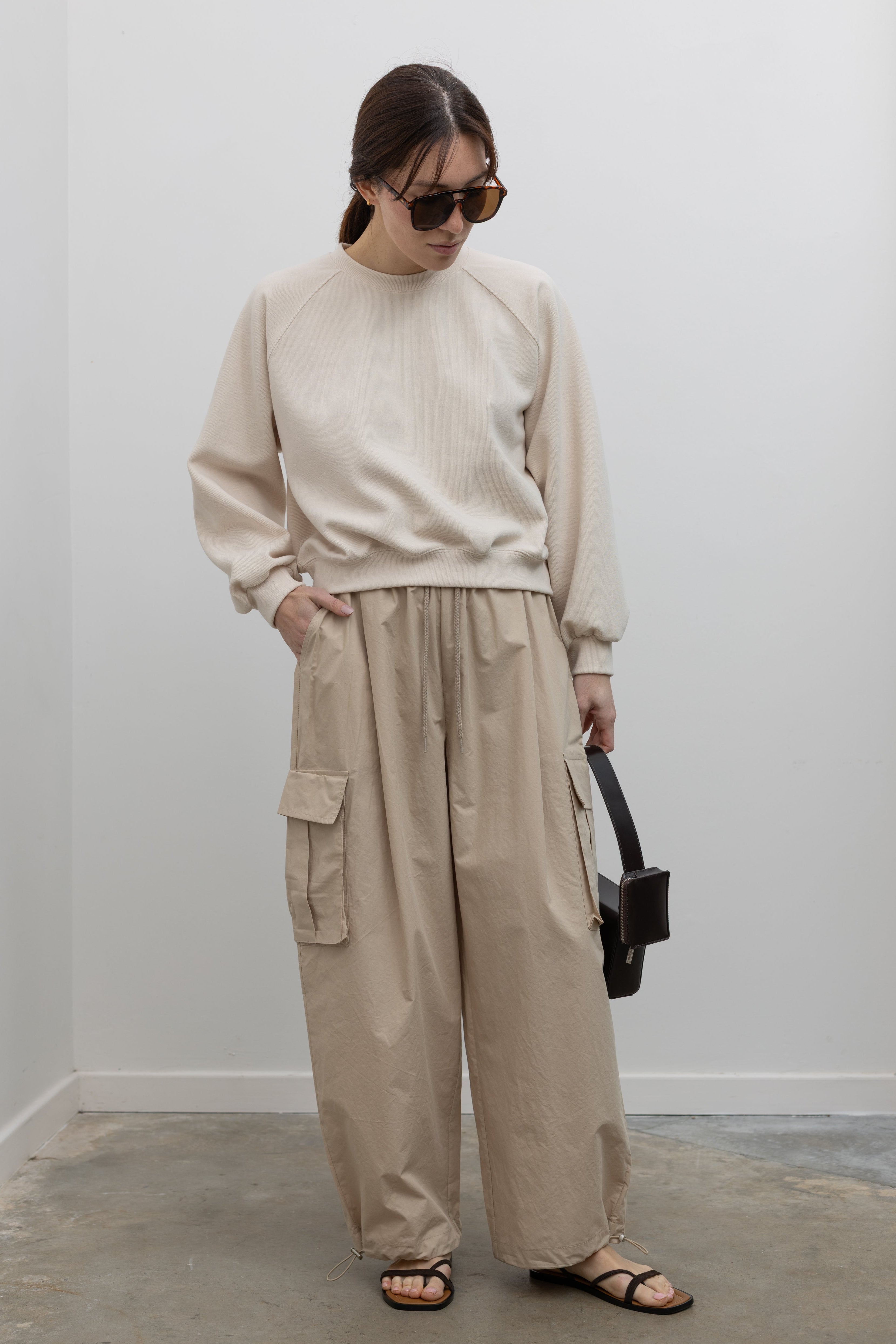Woman wearing Alas Eius Brand Cream Raglan long-sleeved crewneck Sweatshirt with khaki cargo pants and sunglasses at Alas Eius