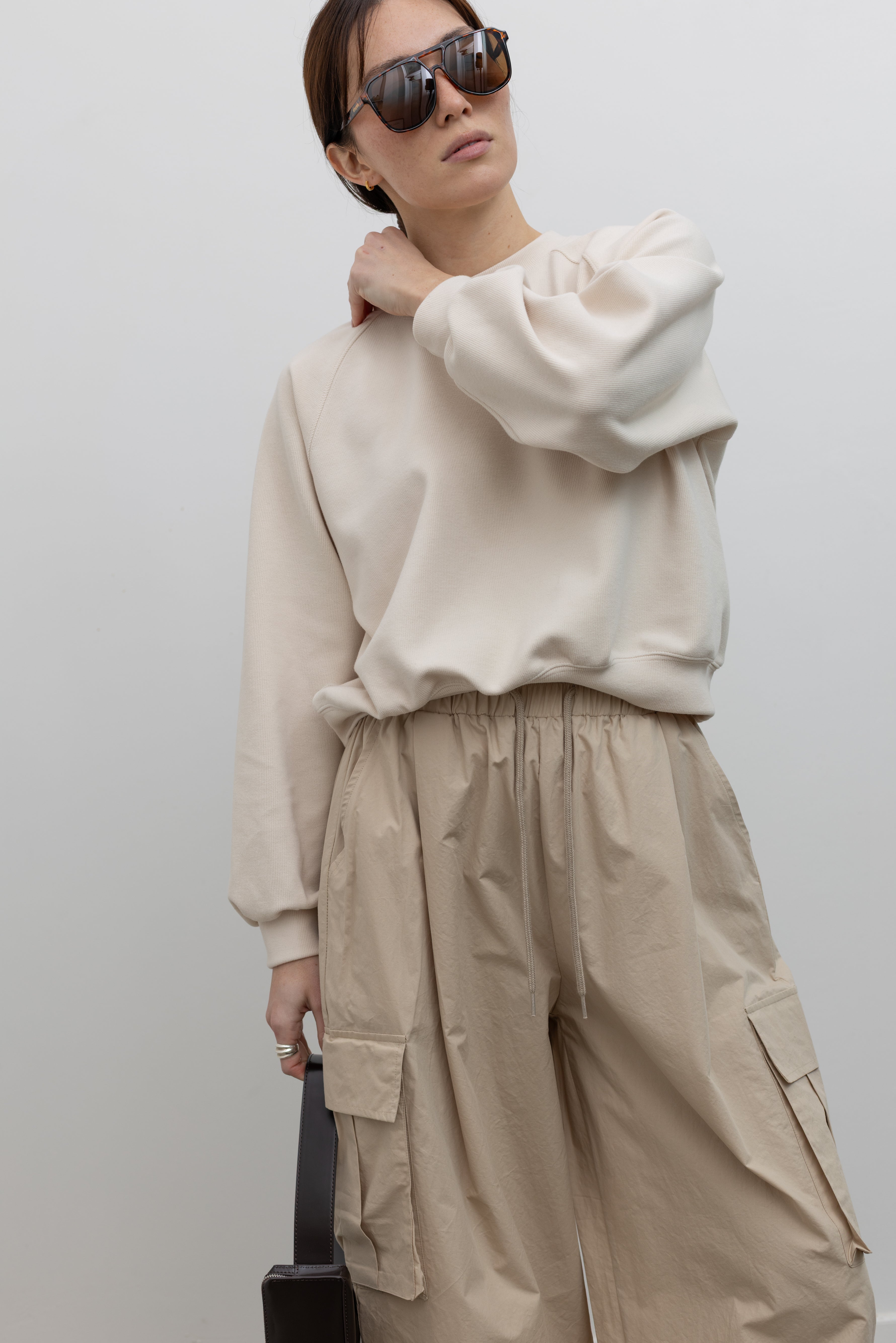 Woman wearing Alas Eius Brand Cream Raglan long-sleeved crewneck Sweatshirt with khaki cargo pants and sunglasses at Alas Eius