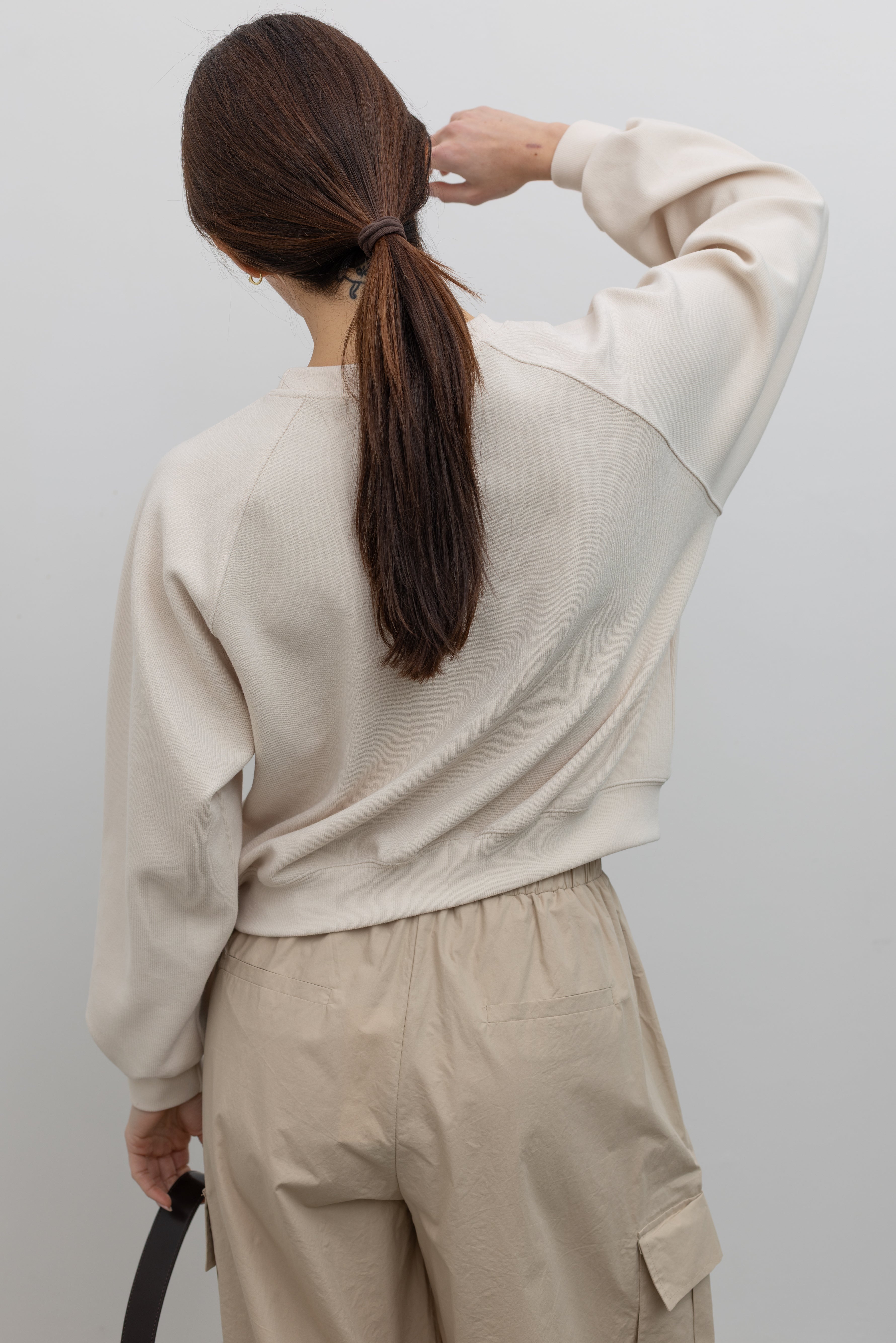 Back view of Woman wearing Alas Eius Brand Cream Raglan long-sleeved crewneck Sweatshirt with khaki cargo pants and sunglasses at Alas Eius