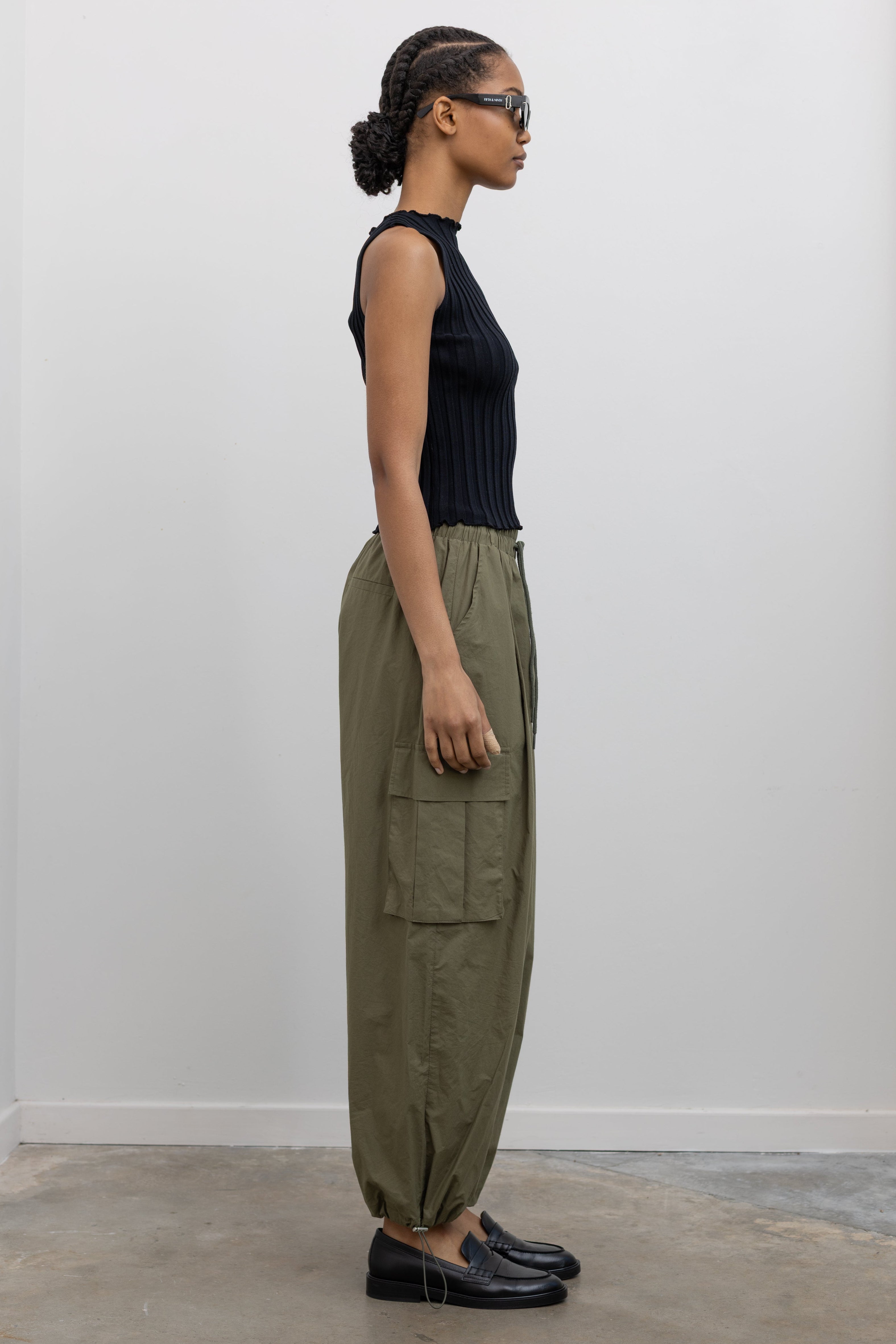 Woman standing wearing everyday fashion in a pair of Alas Eius brand khaki green lightweight cotton wide-leg cargo pants with drawstring ankles and a tie waist and extra pockets at Alas Eius 