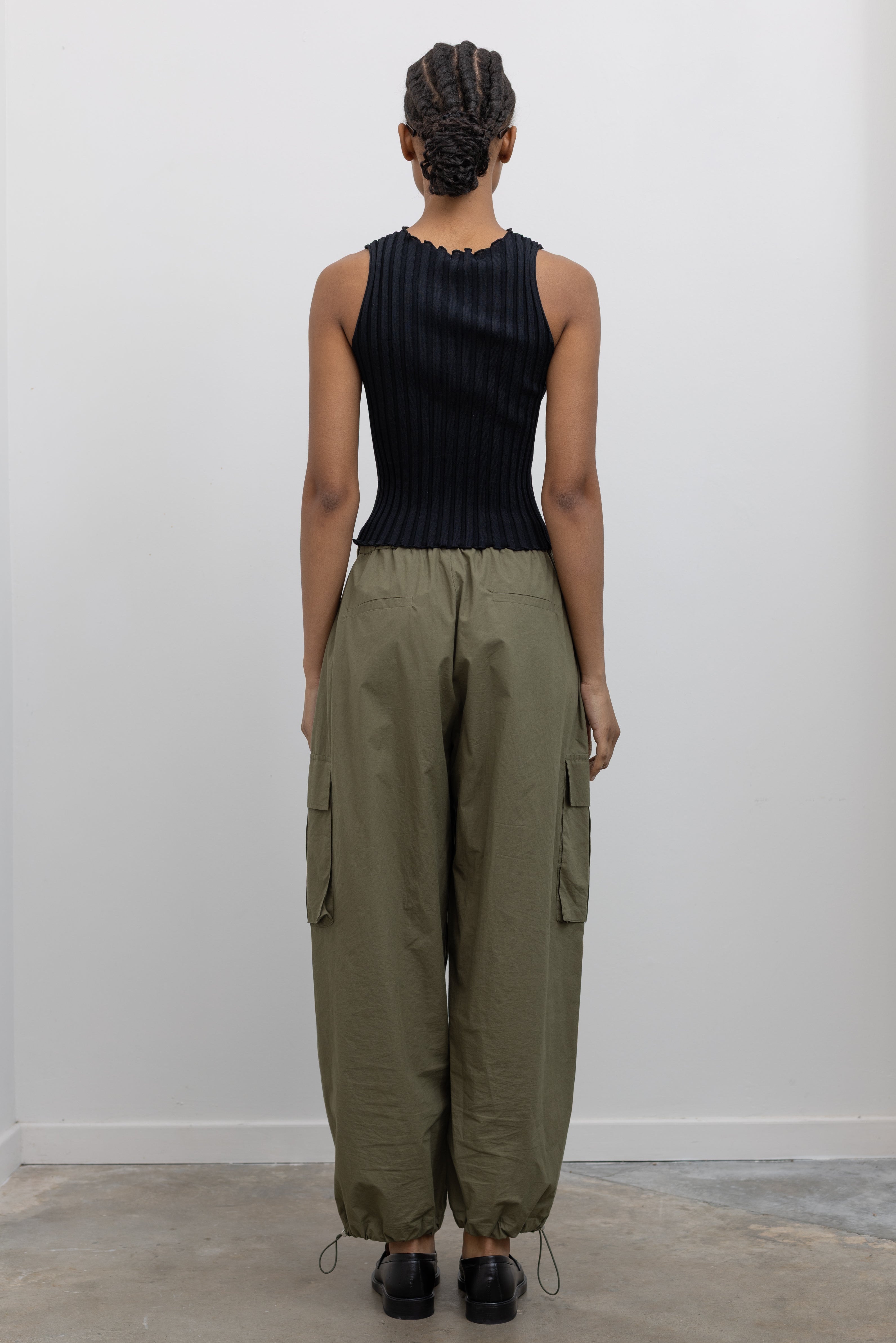 Back view of Woman standing wearing everyday fashion in a pair of Alas Eius brand khaki green lightweight cotton wide-leg cargo pants with drawstring ankles and a tie waist and extra pockets at Alas Eius 
