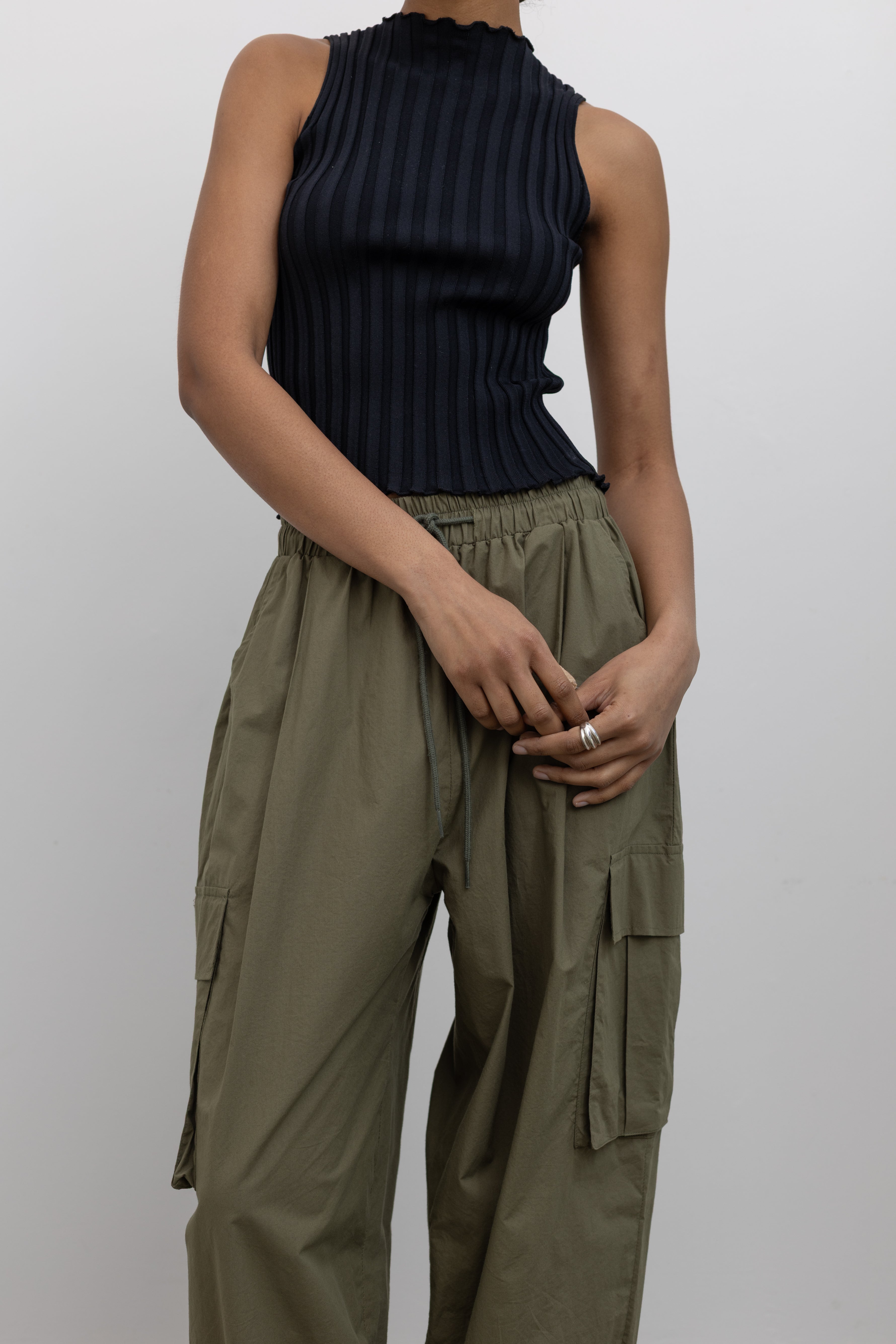 Woman standing wearing everyday fashion in a pair of Alas Eius brand khaki green lightweight cotton wide-leg cargo pants with drawstring ankles and a tie waist and extra pockets at Alas Eius 