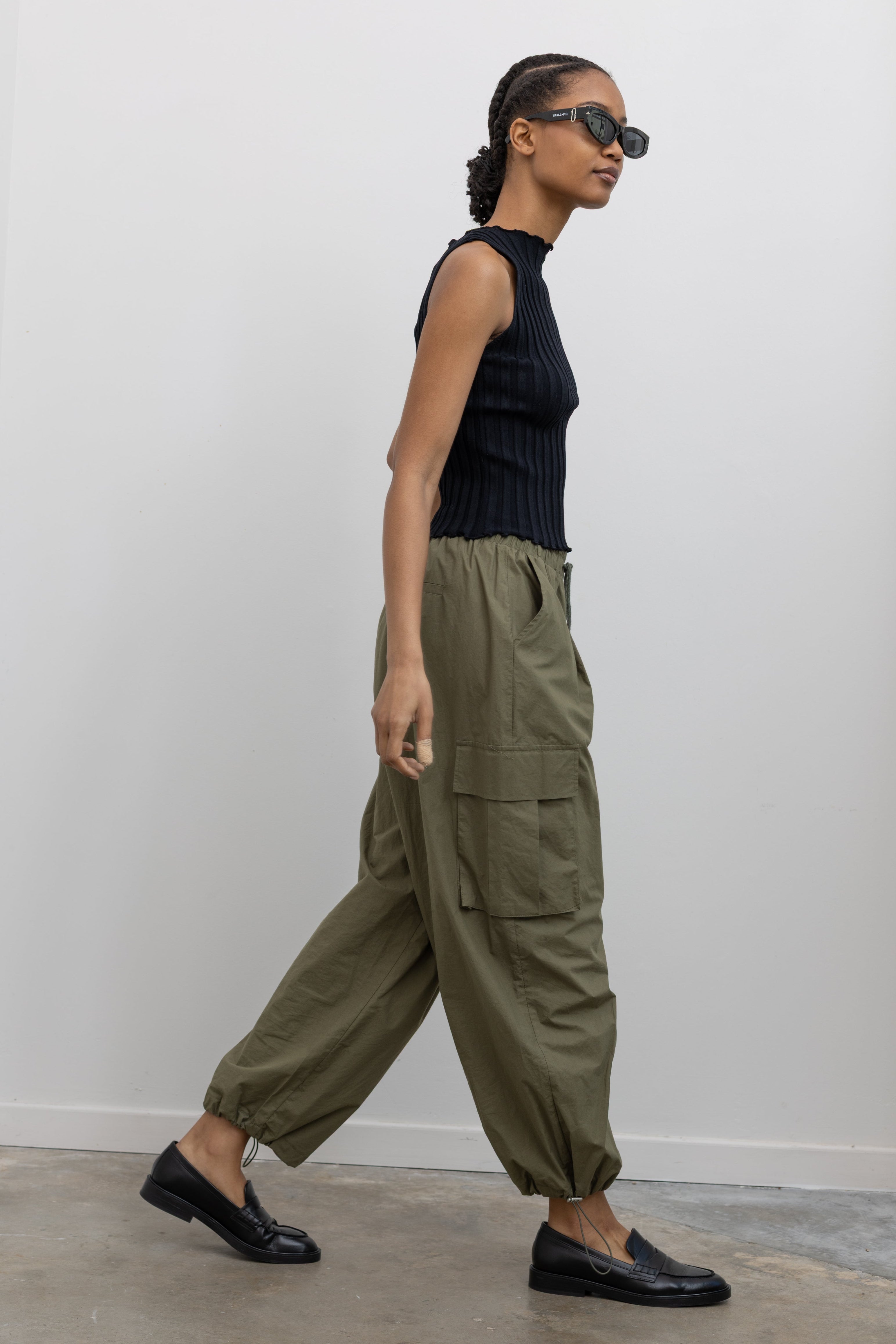 Woman standing wearing everyday fashion in a pair of Alas Eius brand khaki green lightweight cotton wide-leg cargo pants with drawstring ankles and a tie waist and extra pockets at Alas Eius 