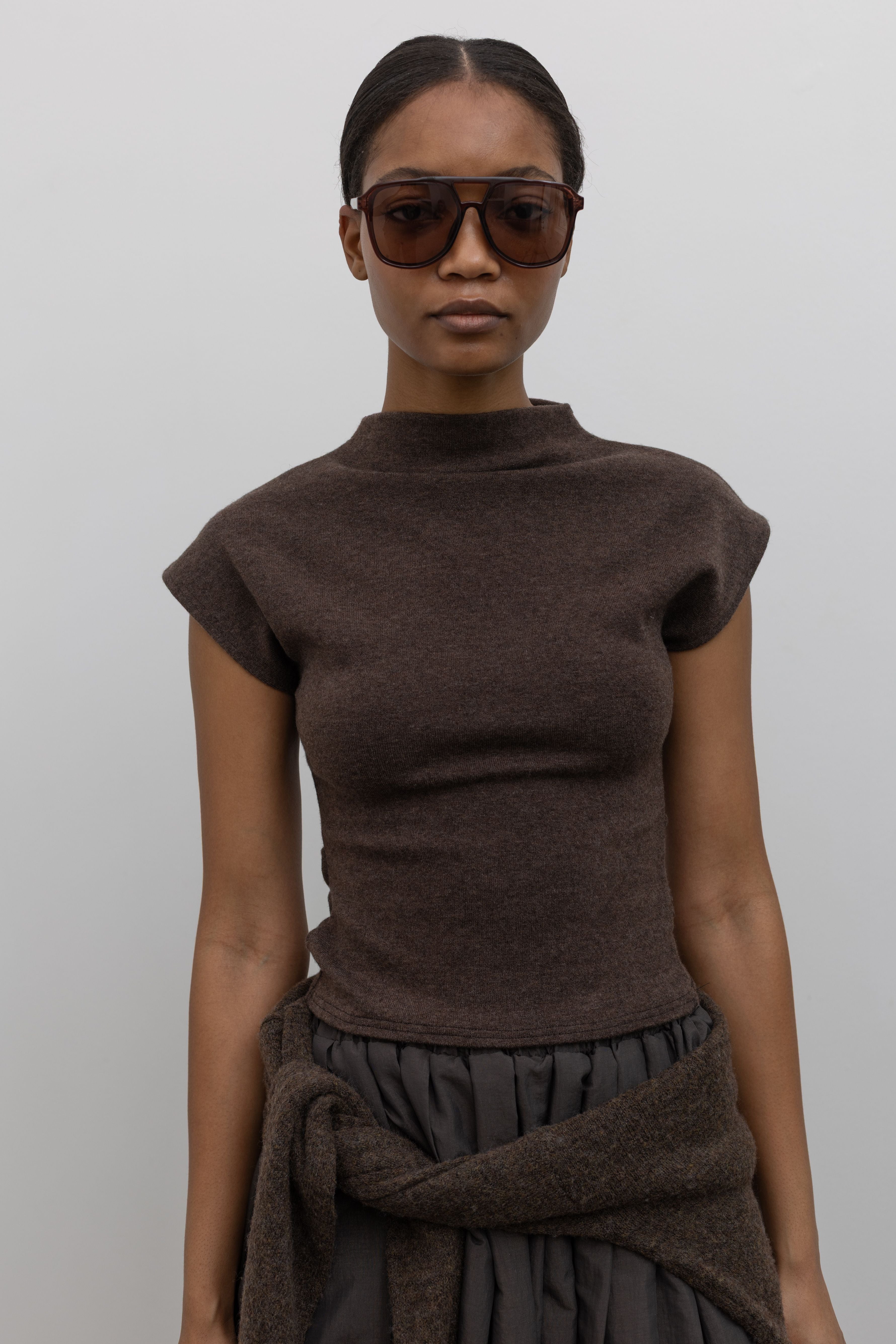 Close-up front view of a woman wearing Contemporary fashion in a Alas Eius label brown mock neck knit slim fit top with flattering cap sleeves at Alas Eius