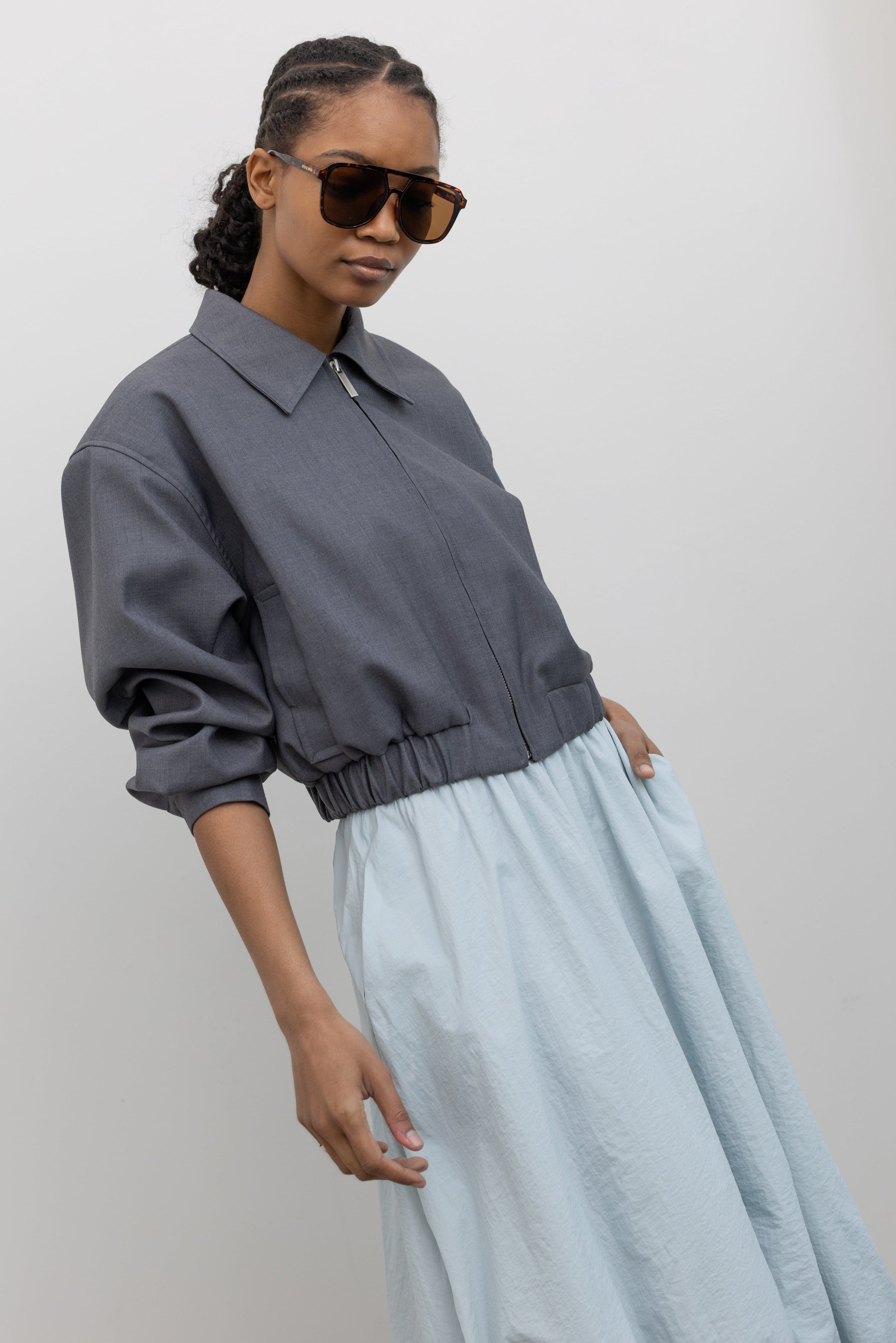 Side view of a woman wearing contemporary womenswear spring fashion in an Alas Eius label charcoal gray cropped tailored zip jacket featuring an elastic hem for a flattering cinched waist at an Alas Eius store. 