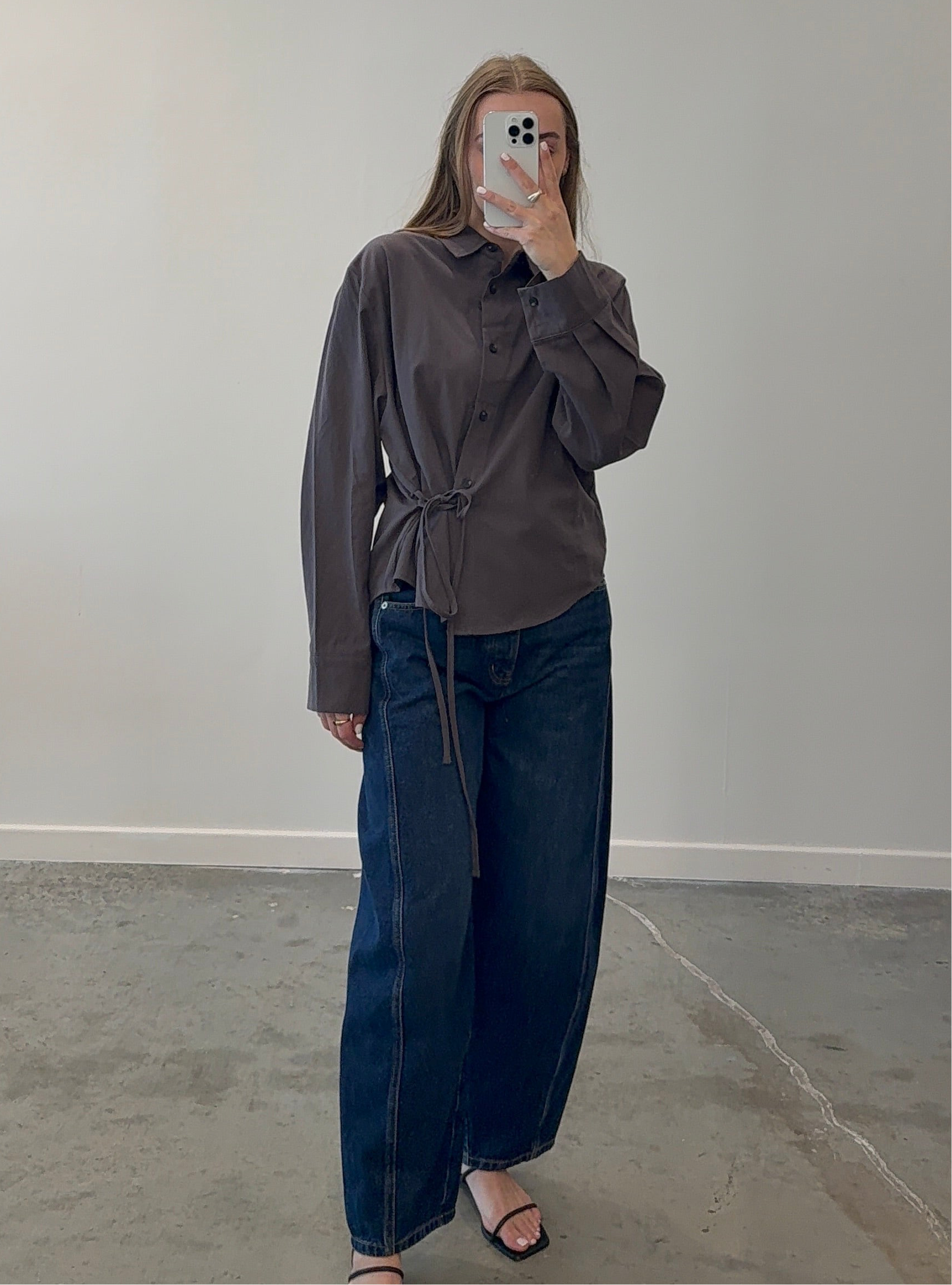 Person wearing a brown shirt and blue jeans against a plain background