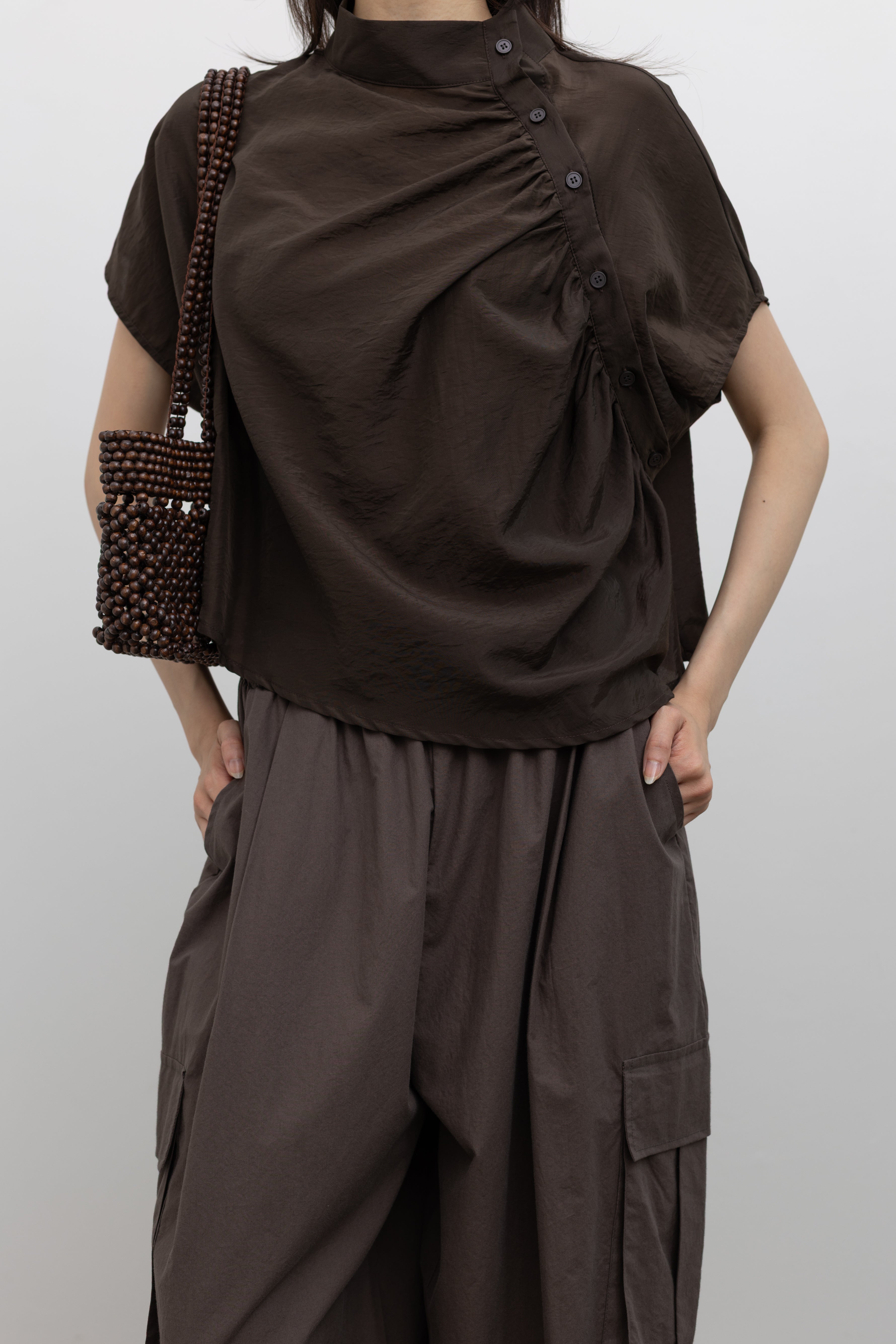 Alas Eius contemporary mock neck top featuring a softly draped silhouette and delicate side button detailing, styled as a versatile women’s fashion essential for modern minimalist wardrobes at Alas Eius