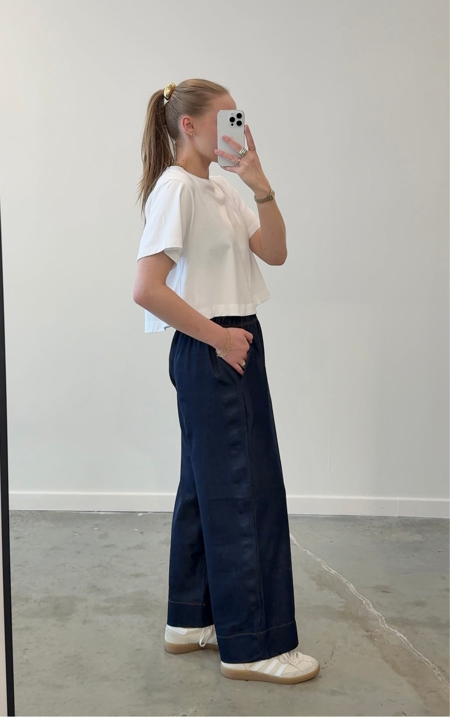Person wearing a white top and navy wide-leg pants taking a mirror selfie.