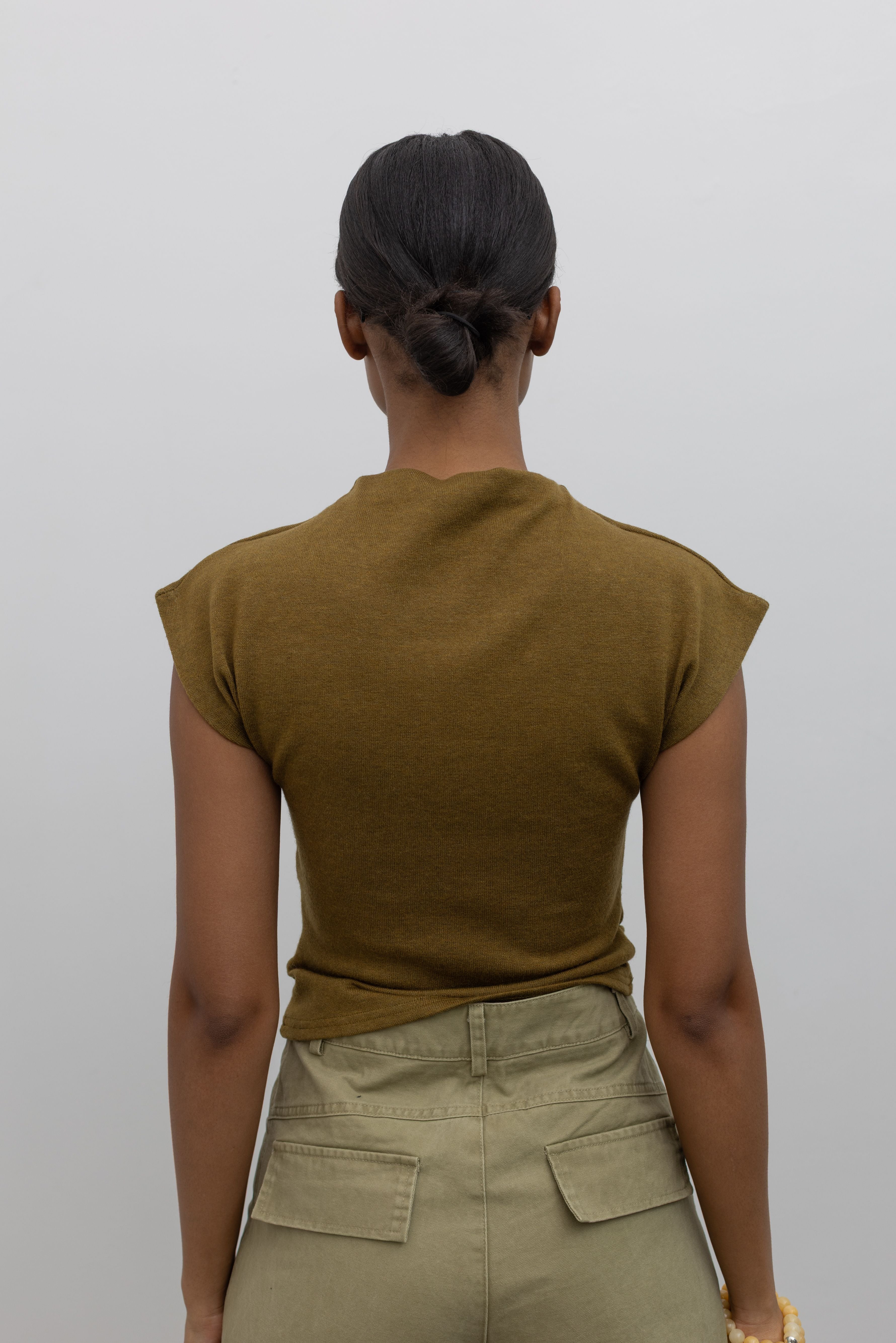 Close-up back view of a woman wearing refined womens fashion in a Alas Eius label olive mock neck knit slim fit top with flattering cap sleeves at Alas Eius