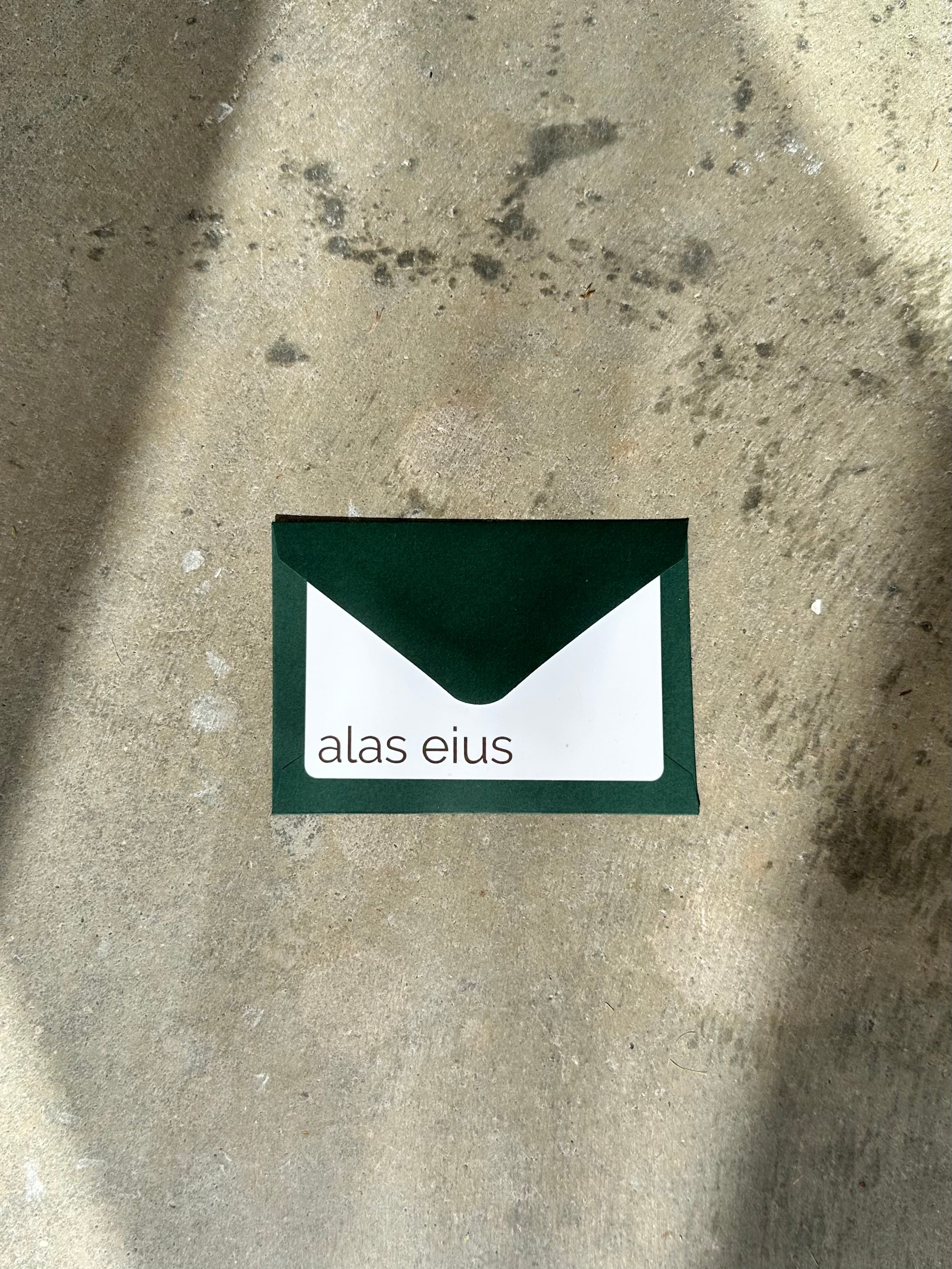 Alas Eius Gift Card wtih green envelope on concrete background 