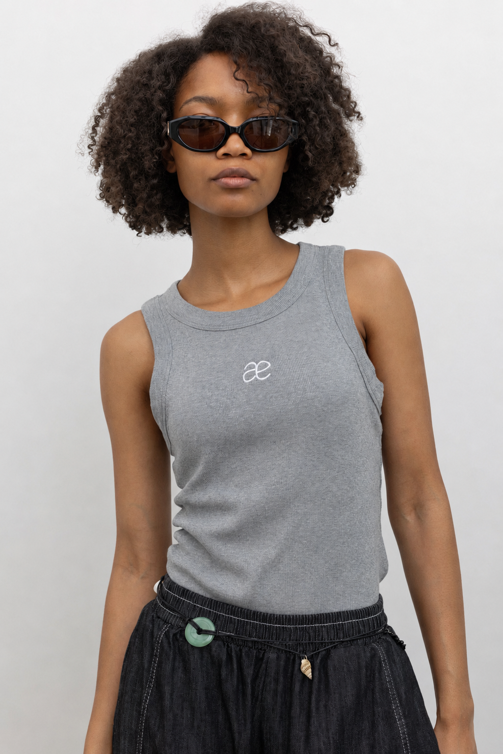 Alas Eius label gray cotton blend ribbed racerback tank top with contrasting embroidered AE logo on chest paired with Alas Eius Black Contrast Stitch Barrel Jeans. 