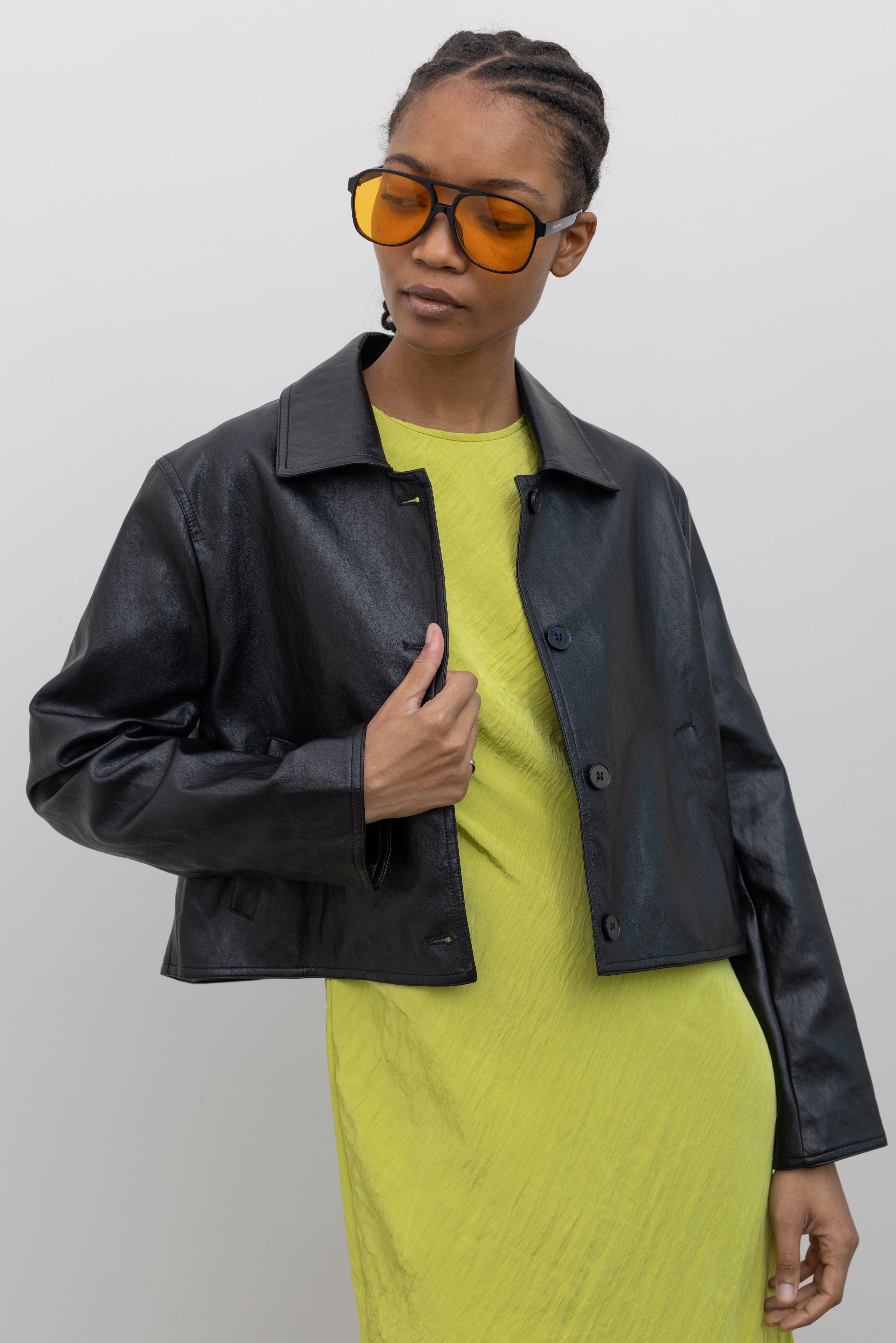 Woman posing wearing chic and refined Alas Eius Label Black Cropped Vegan Leather Collared Jacket with a chartreuse dress at Alas Eius.  