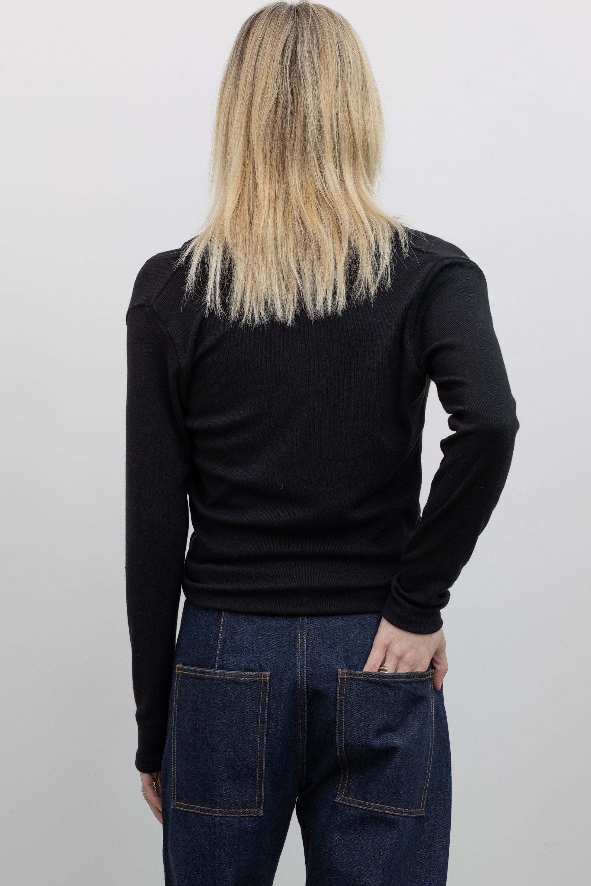 Back view of Woman wearing Alas Euis label deep v-neck double layer long sleeve black knit top with mock neck and open shoulders with dark wash Tibi jeans at alas eius