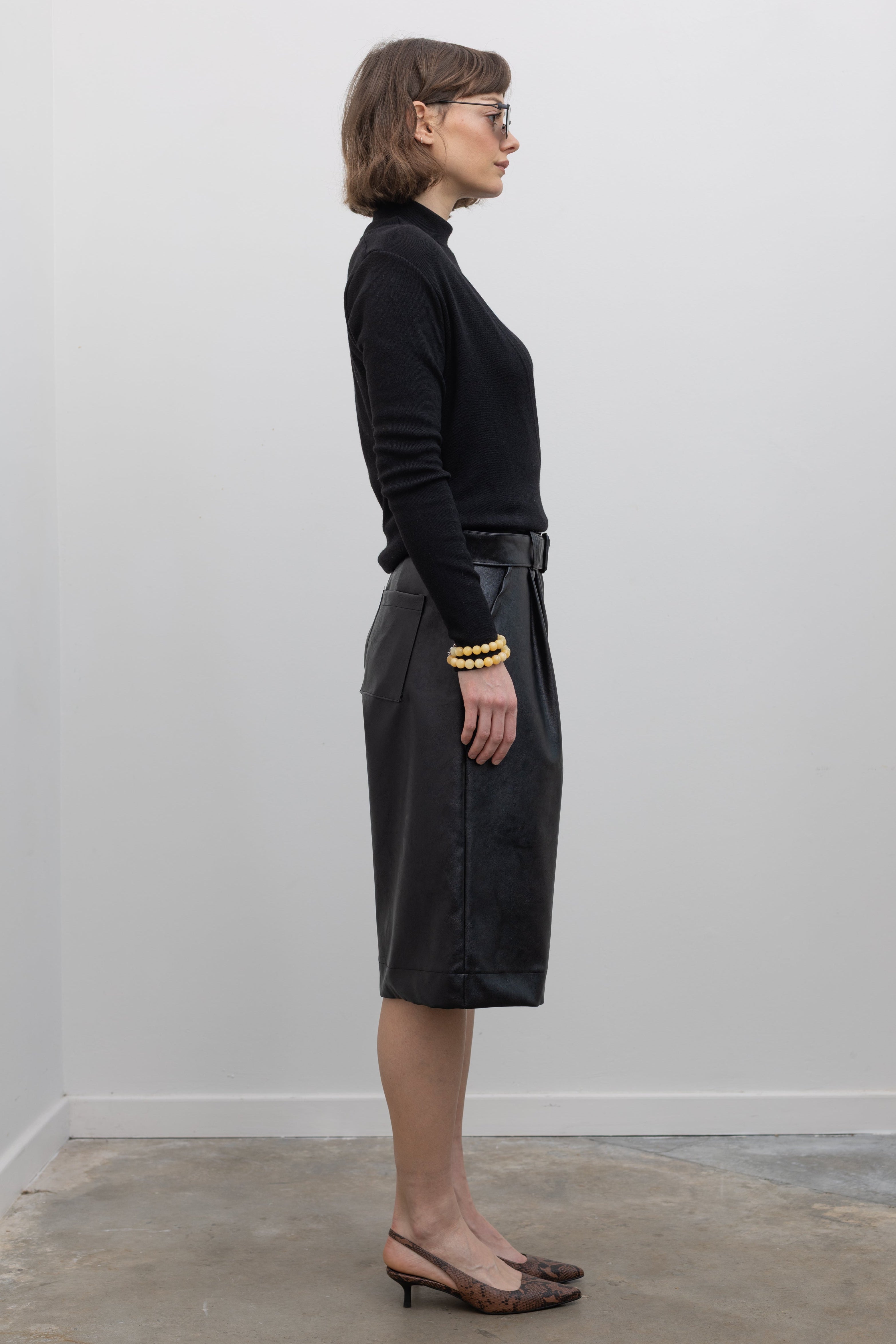 Right side view of Woman wearing Alas Euis label deep v-neck double layer long sleeve black knit top with mock neck and open shoulders at alas eius