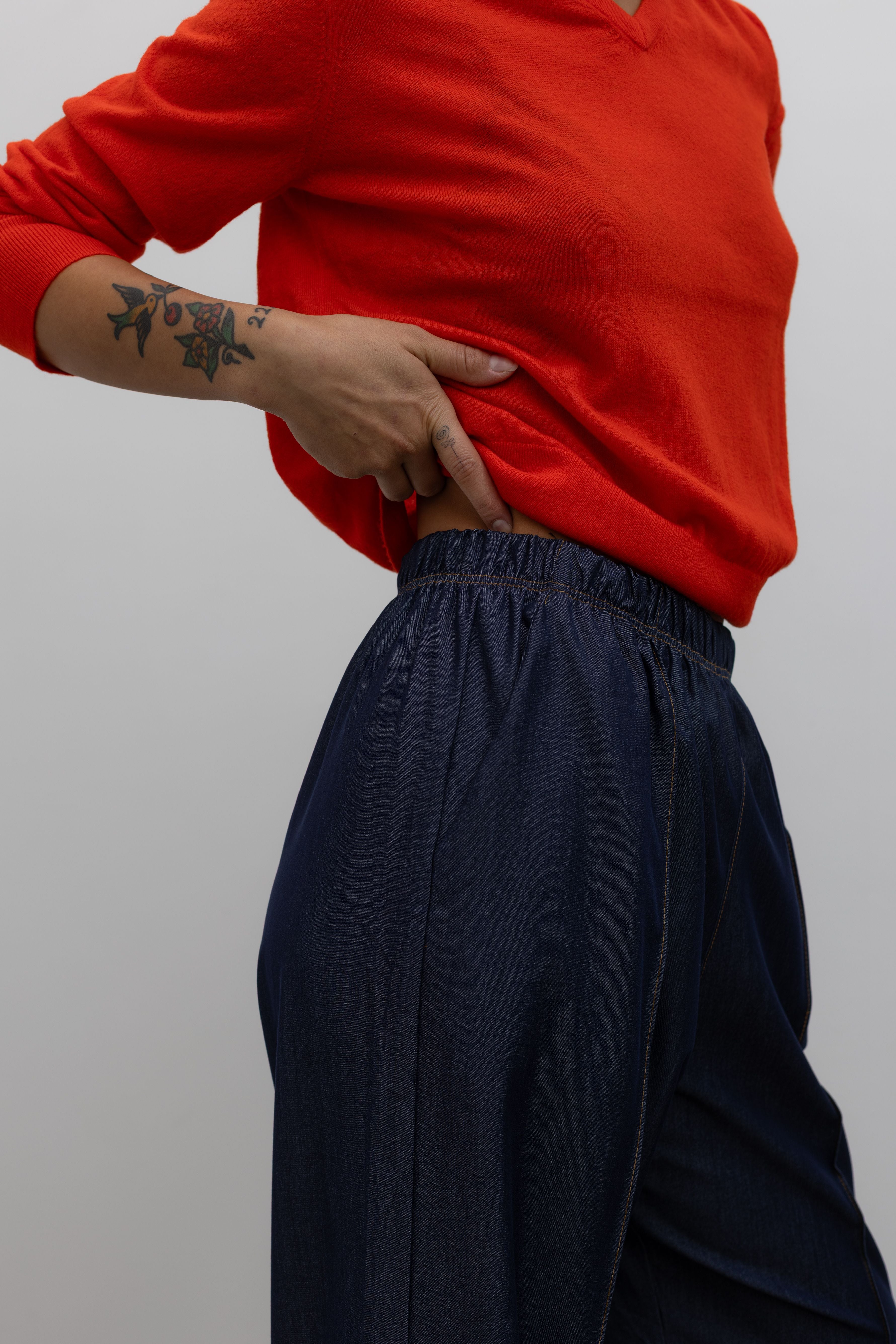 Detailed product view of Woman standing wearing an everyday outfit with a Tibi Red v-neck cashmere sweater and Alas Eius Label Tencel Blend Dark Wash Tailored Wide Leg Pull On Pants at Alas Eius. 