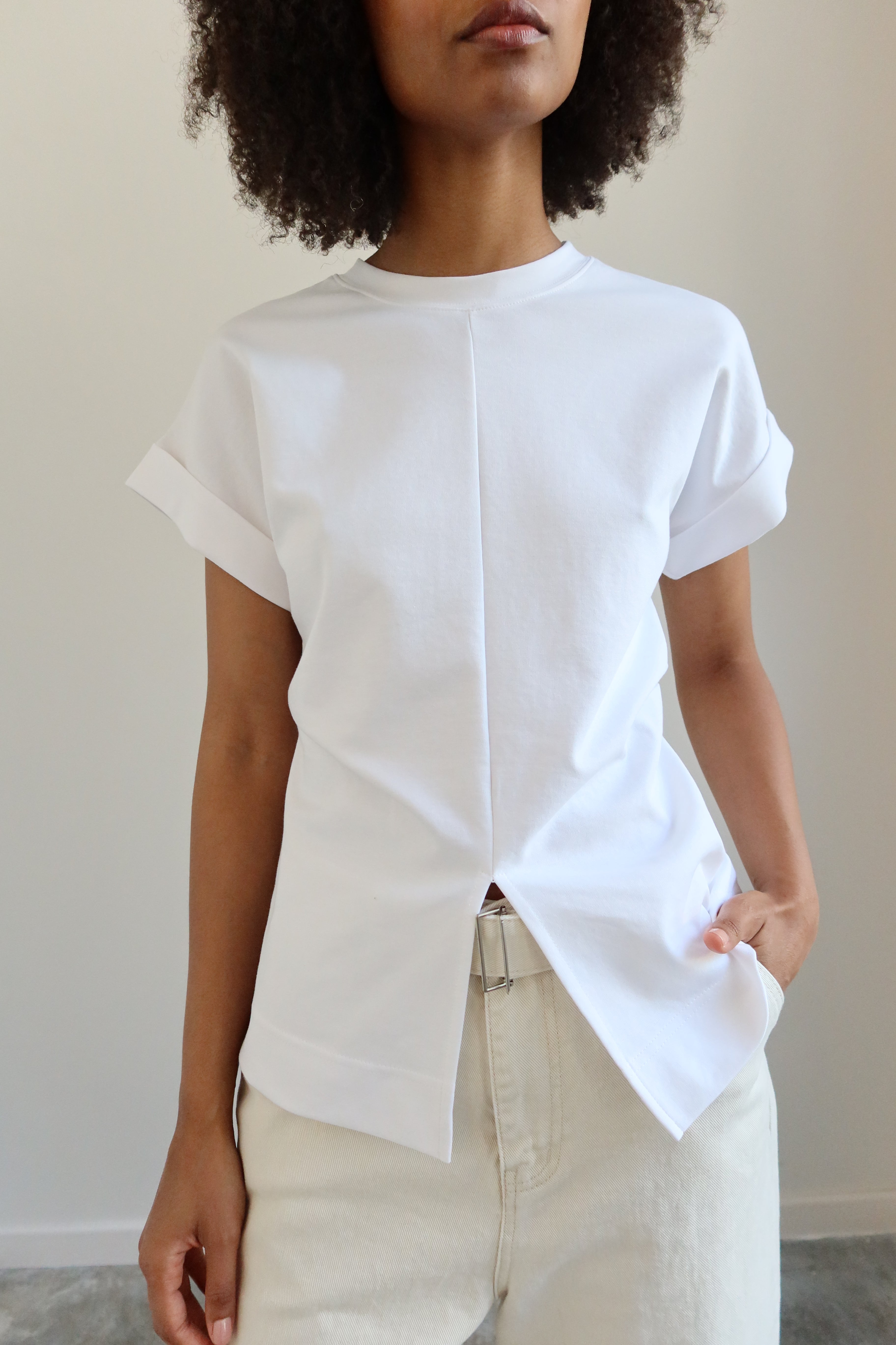 Detailed product view of Woman standing wearing capsule wardrobe essential in an Alas Eius Label White Cinched Waist Deep V Cutout Hem Top with ivory cropped wide leg pants at Alas Eius 