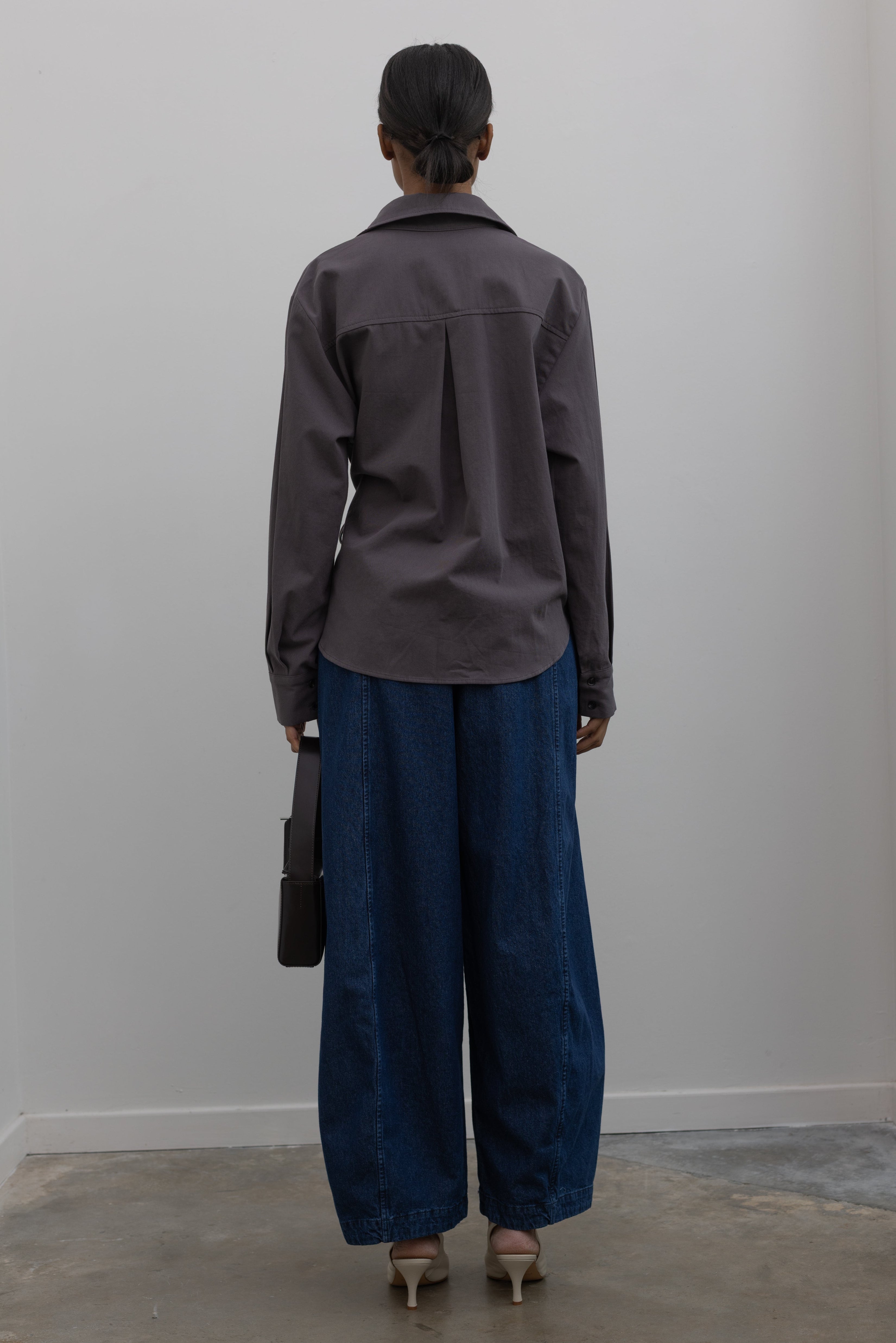 Back view of Woman wearing capsule wardrobe essential outfit in an elegant and flattering Alas Eius label gray brushed cotton cinched waist button down collared long sleeve top with Le Bon Shoppe Denim Blue Cotton Parachute Pants paired white leather slingback heels and a St. Agni shiny brown leather bag at Alas Eius. 