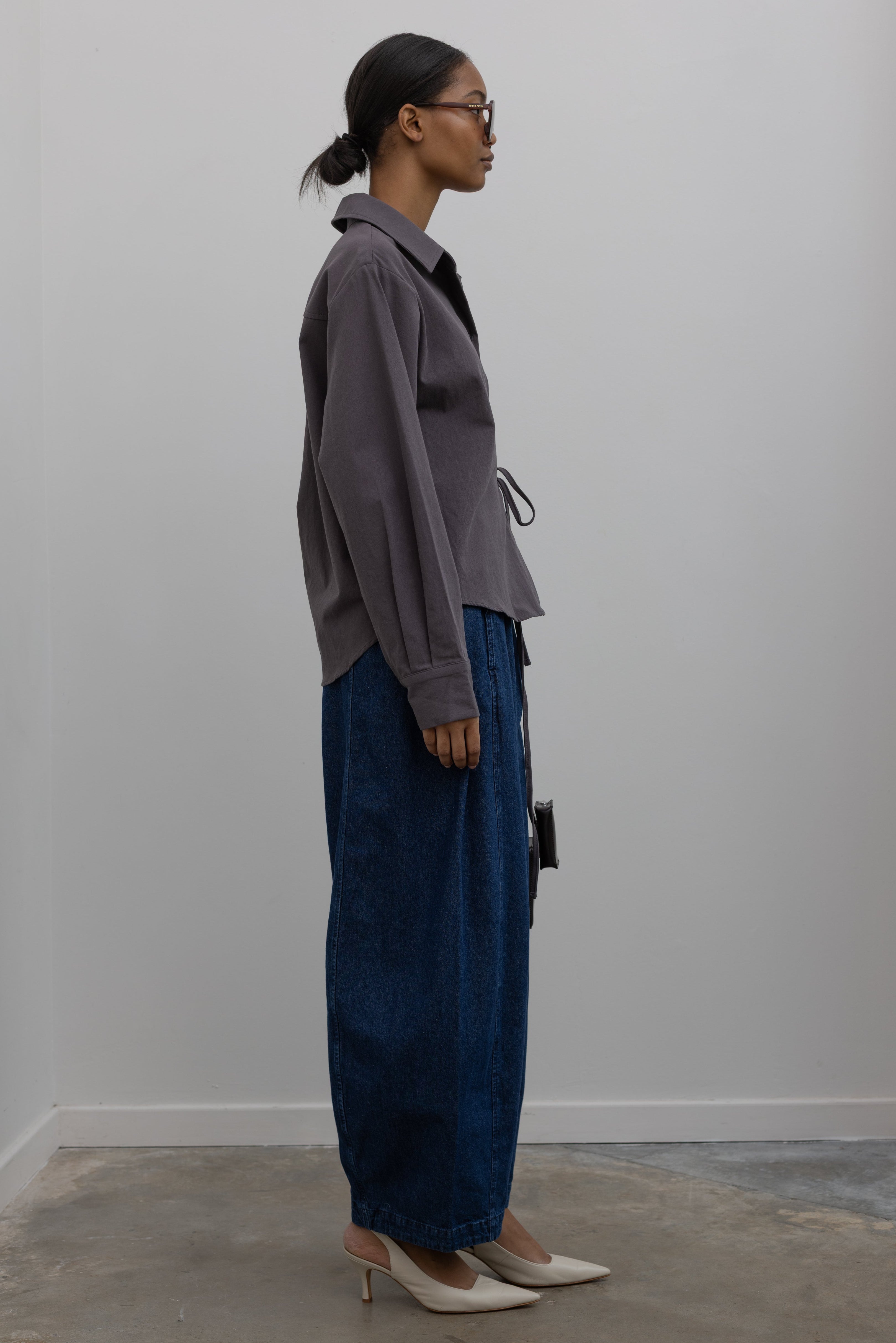 Back view of Woman wearing capsule wardrobe essential outfit in an elegant and flattering Alas Eius label gray brushed cotton cinched waist button down collared long sleeve top with Le Bon Shoppe Denim Blue Cotton Parachute Pants paired white leather slingback heels and a St. Agni shiny brown leather bag at Alas Eius. 