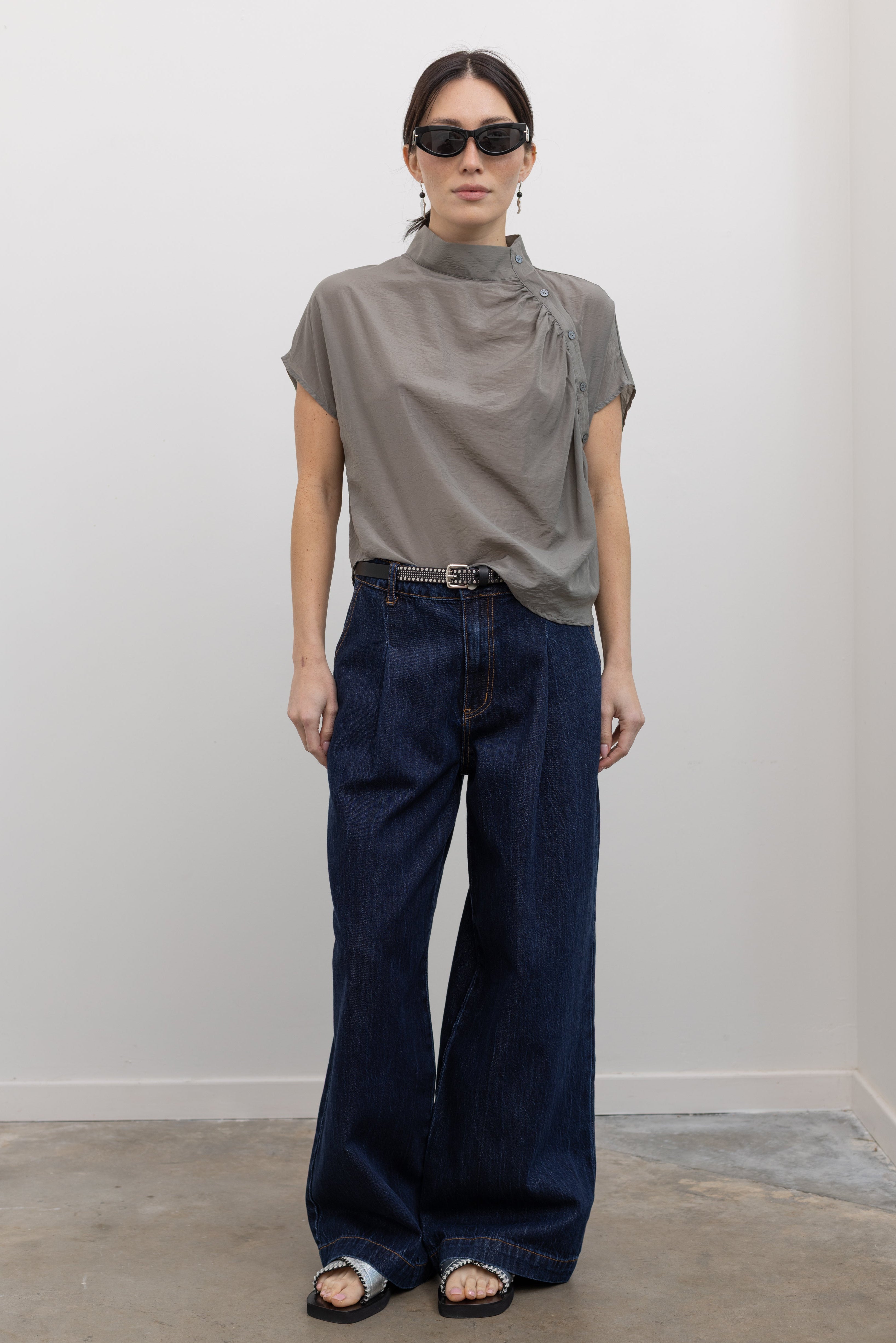 Woman wearing feminine and modest spring fashion in an Alas Eius label light gray organza asymmetrical button mock neck top with dark wash denim jeans at an Alas Eius store. 