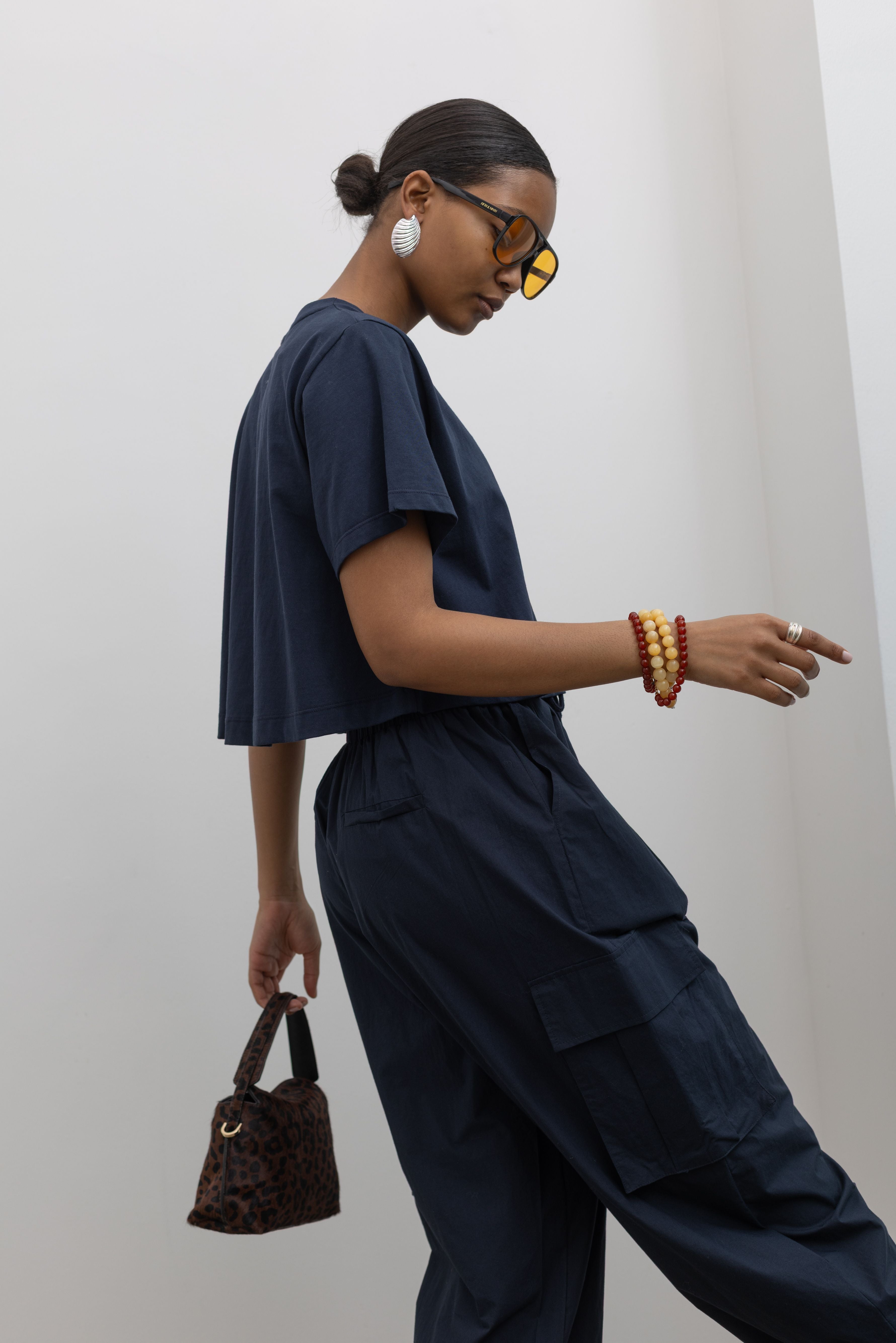 Woman standing wearing everyday essential style in an Alas Eius Label Navy Blue Relaxed Cropped Short Sleeved T-Shirt with Navy Blue Cargo Pants and accessories at Alas Eius.