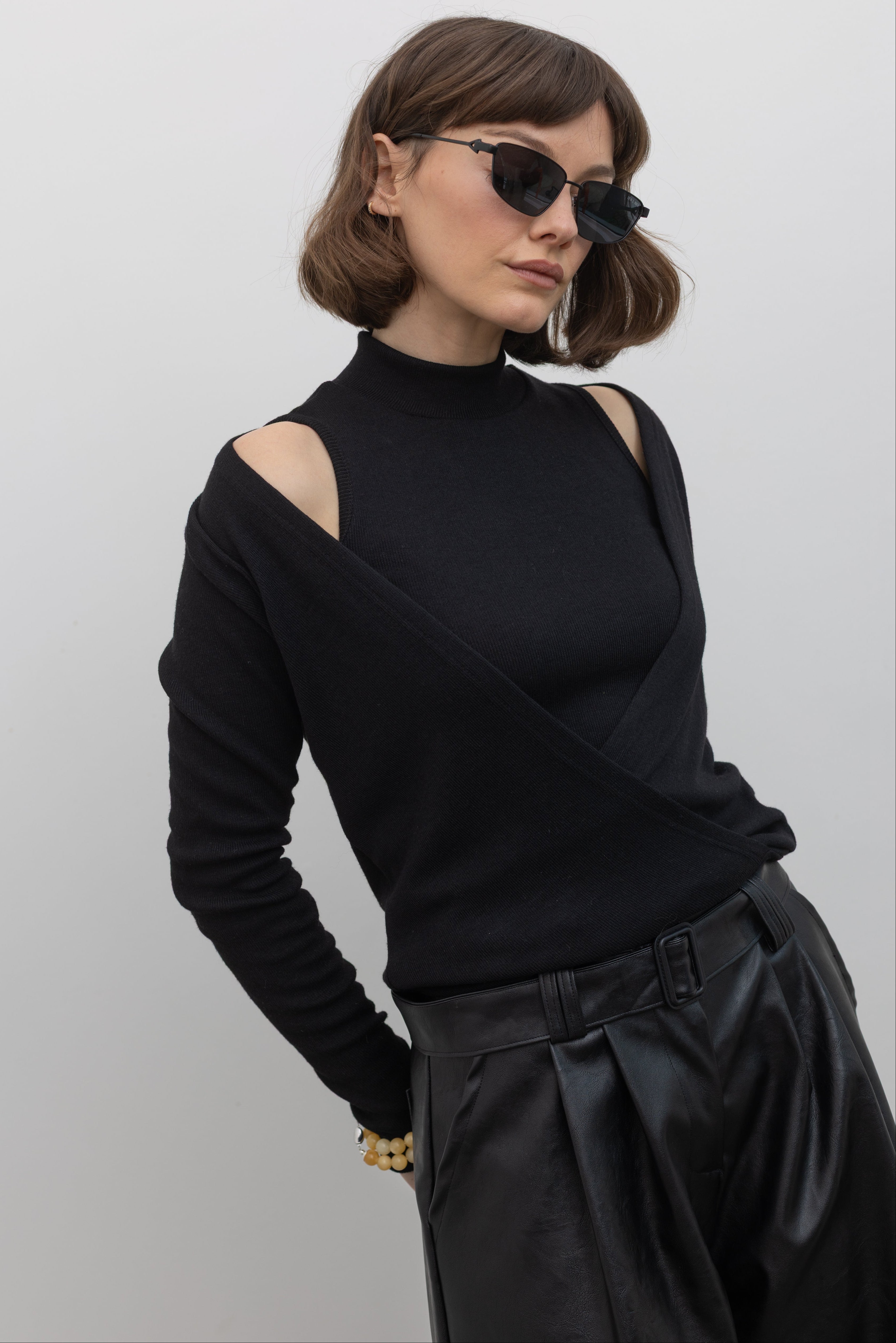 Woman wearing contemporary Alas Euis label double layer long sleeve knit top with mock neck and open shoulders at an Alas Eius store. 