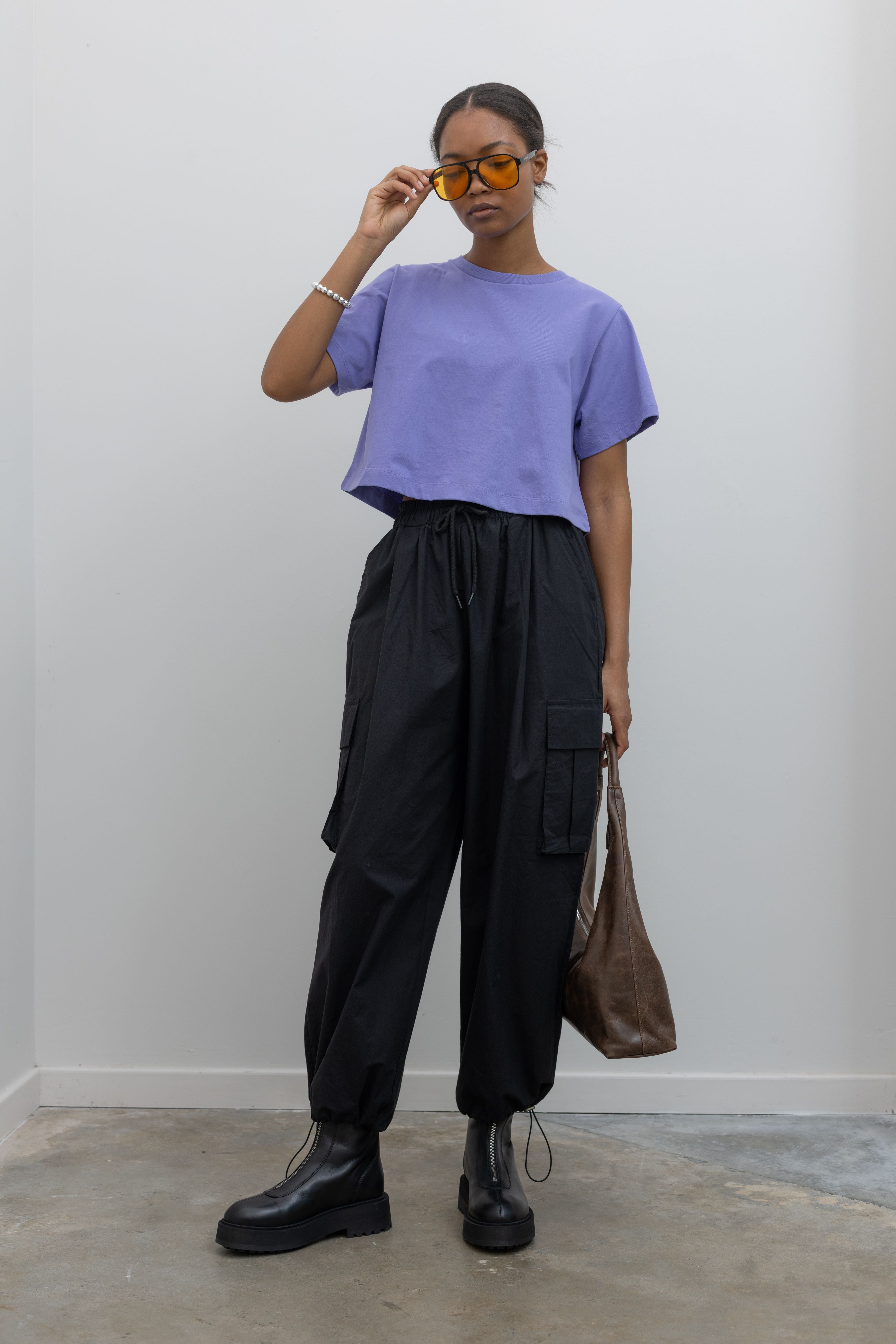 Woman standing wearing must-have capsule wardrobe essential in an Alas Eius Label Lavender Relaxed Boxy Cropped T-Shirt with black cargo pants and platform zip boots at Alas Eius 