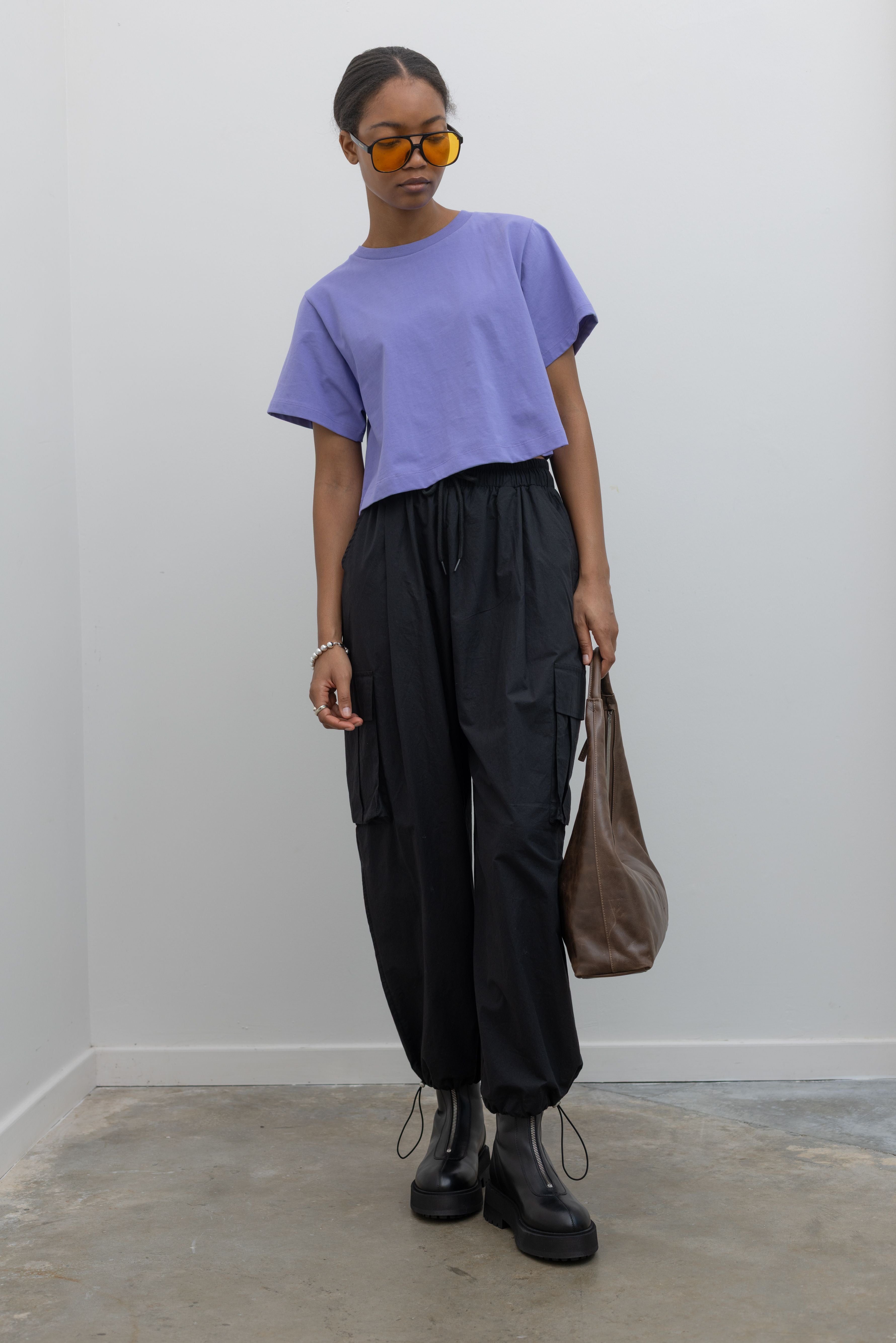 Woman standing wearing must-have capsule wardrobe essential in an Alas Eius Label Lavender Relaxed Boxy Cropped T-Shirt with black cargo pants and platform zip boots at Alas Eius 