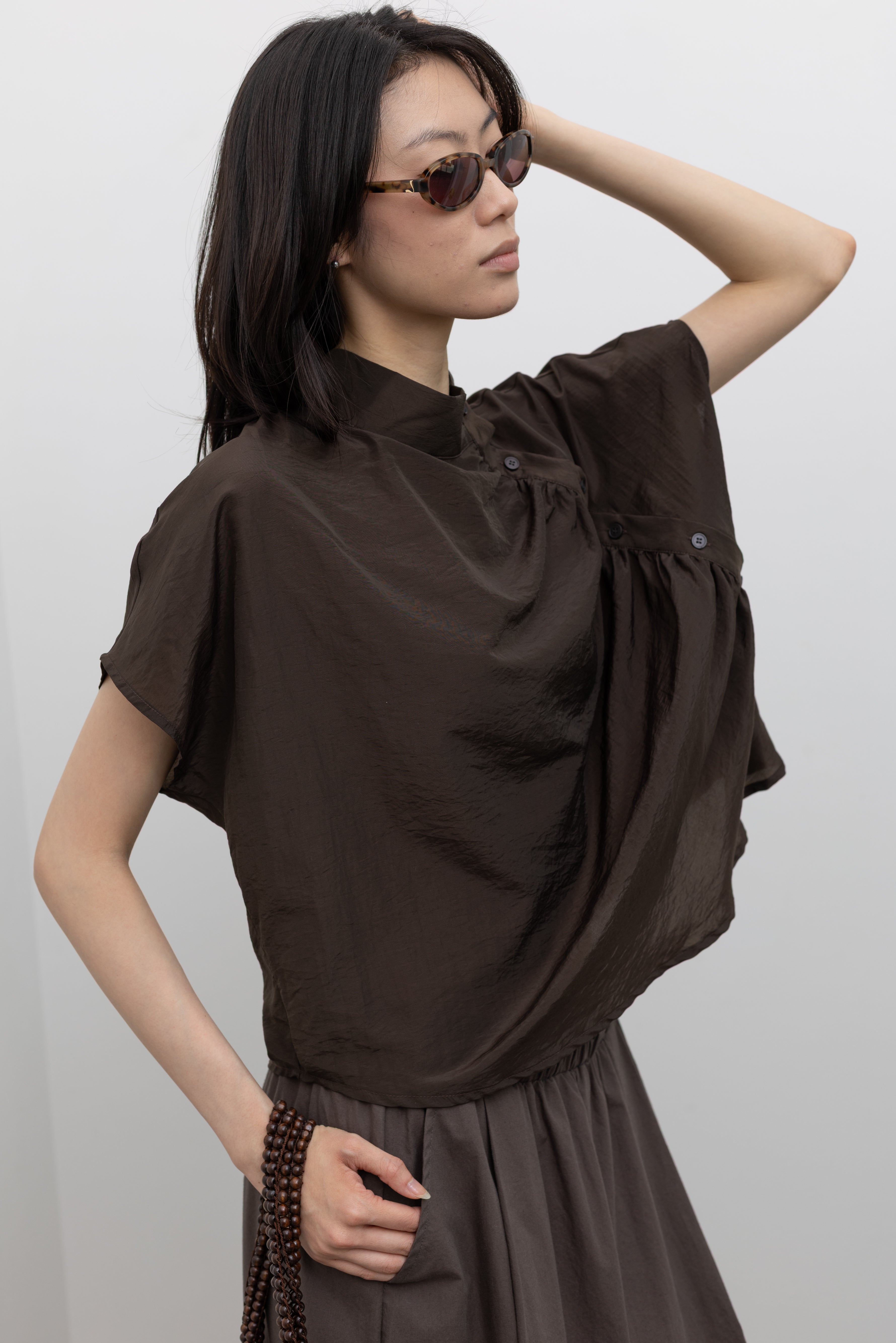 Alas Eius sculptural mock neck top featuring fluid drape, relaxed silhouette, and refined side button accents, styled as a chic women’s fashion blouse for contemporary polished outfits at Alas Eius