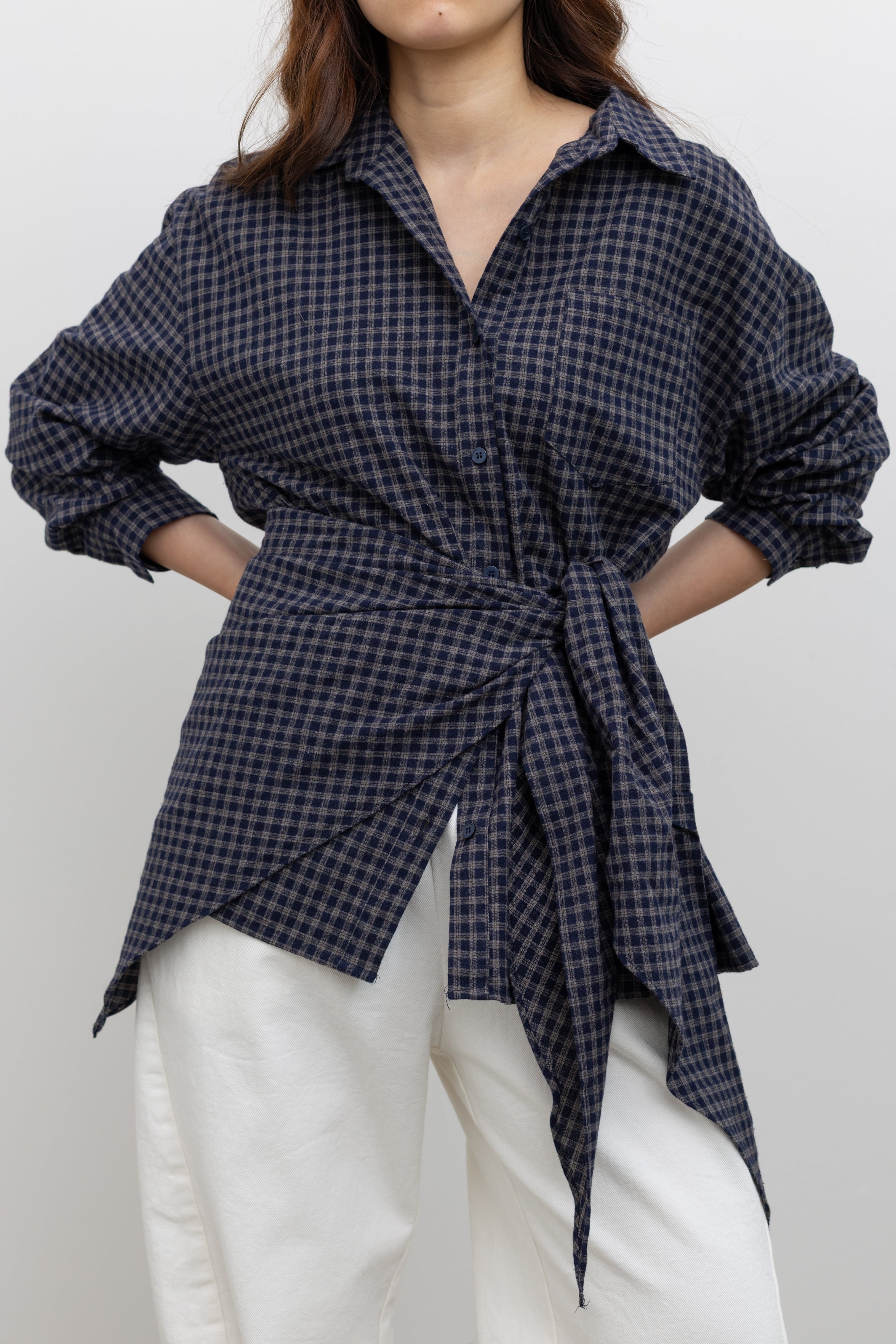 Woman wearing Alas Eius label navy blue and tan cotton checkered plaid button-down shirt with a relaxed fit and matching detachable triangle scarf, styled with wide-leg white denim for a modern elevated look.
